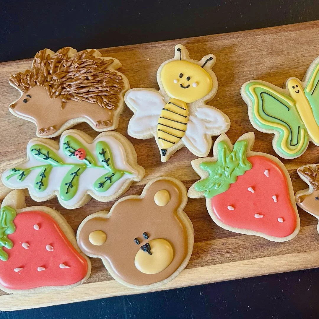 Decorated sugar cookies on a wooden tray, including a lion, a bee, butterflies, strawberries, and a bear.