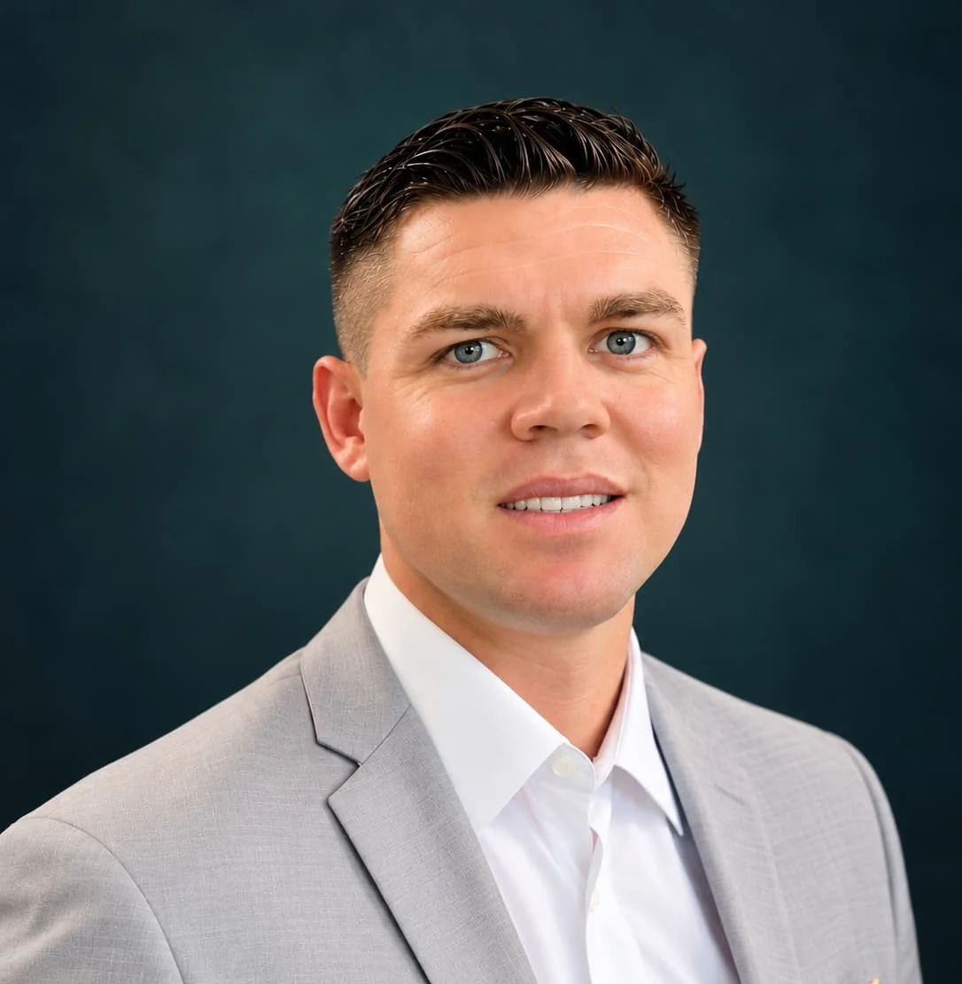 Professional headshot of a smiling man in a light gray suit and white shirt against a dark blue background