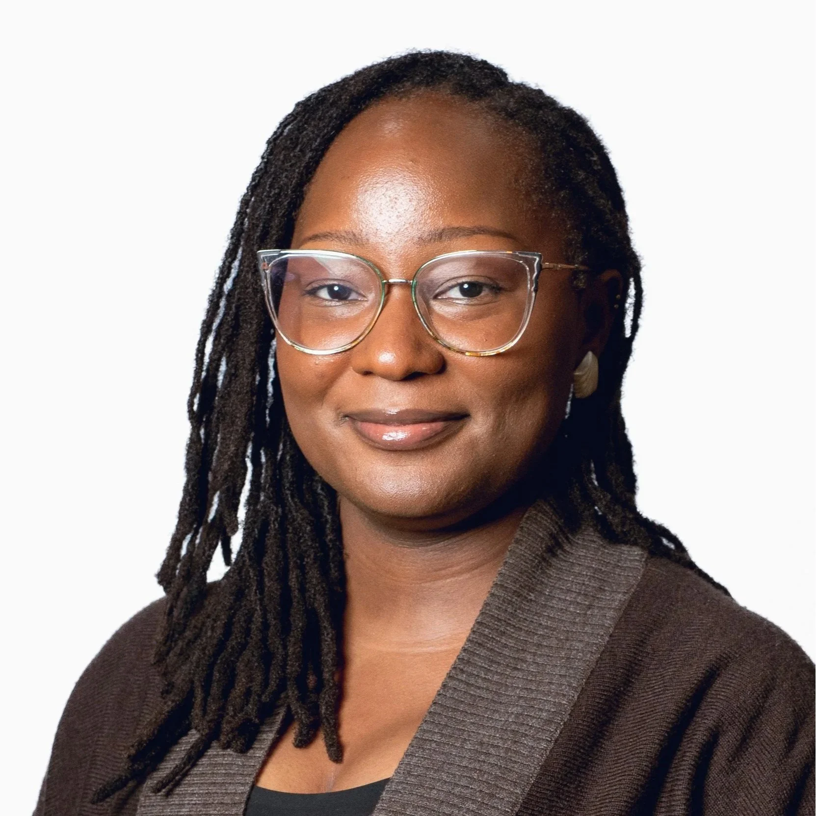 Professional headshot of a Black woman with locs and glasses, wearing a brown sweater.