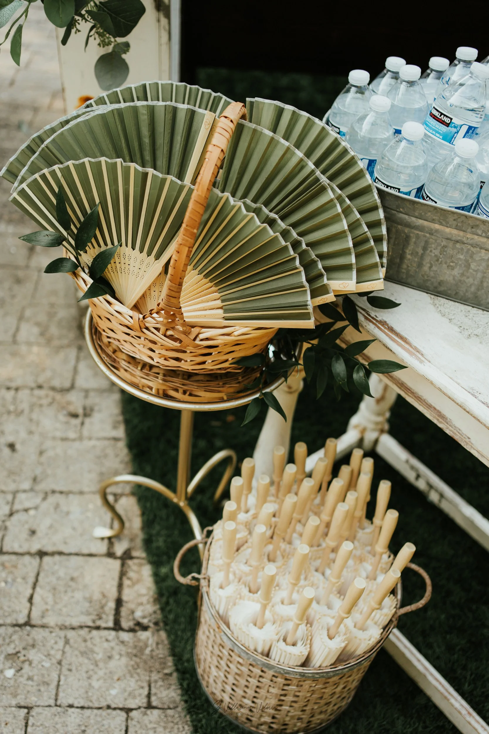 Basket of green paper fans, a bucket of bamboo cocktail stirrers, and bottles of water.