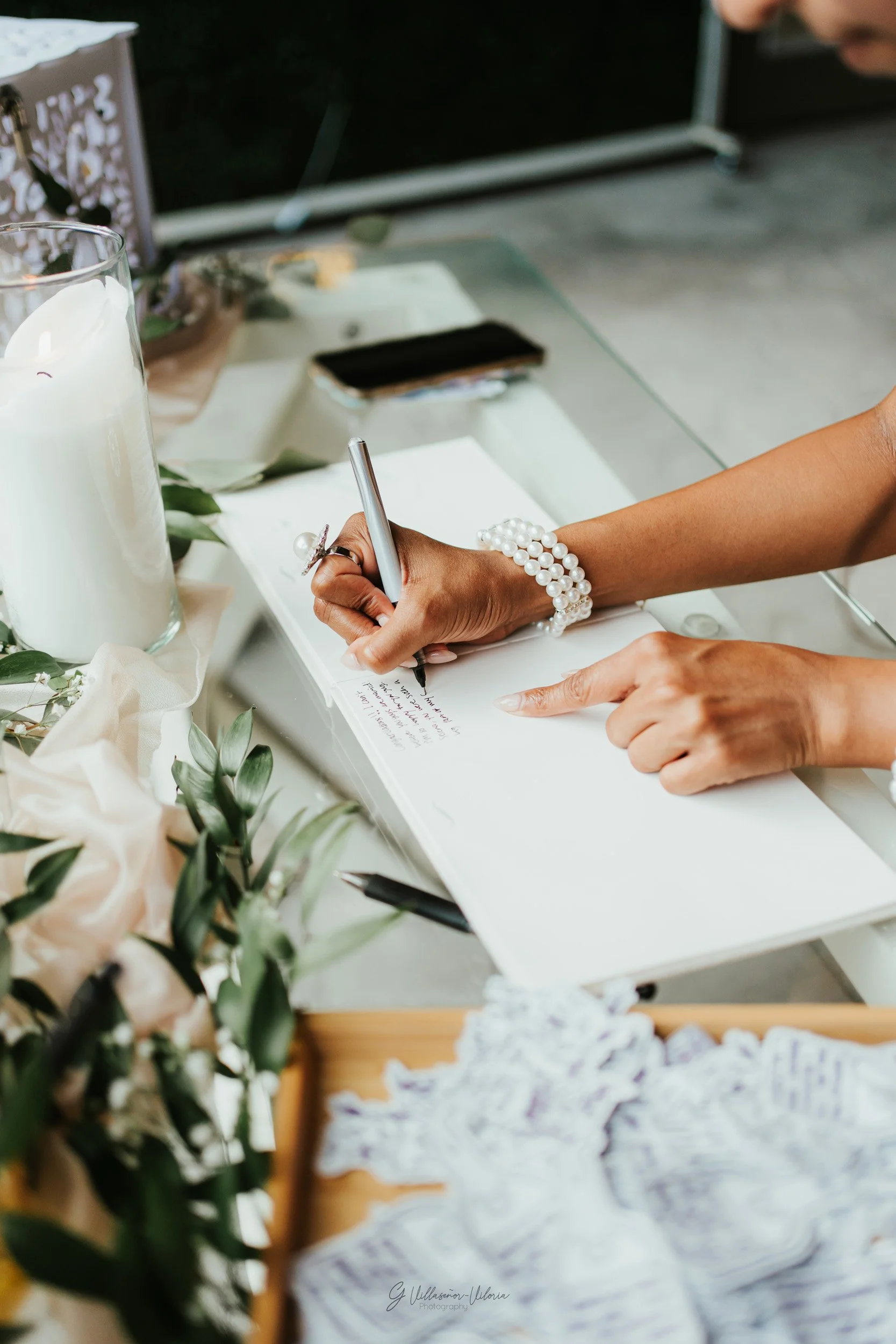 Person signing a guest book at a wedding or special event, surrounded by flowers and candles.
