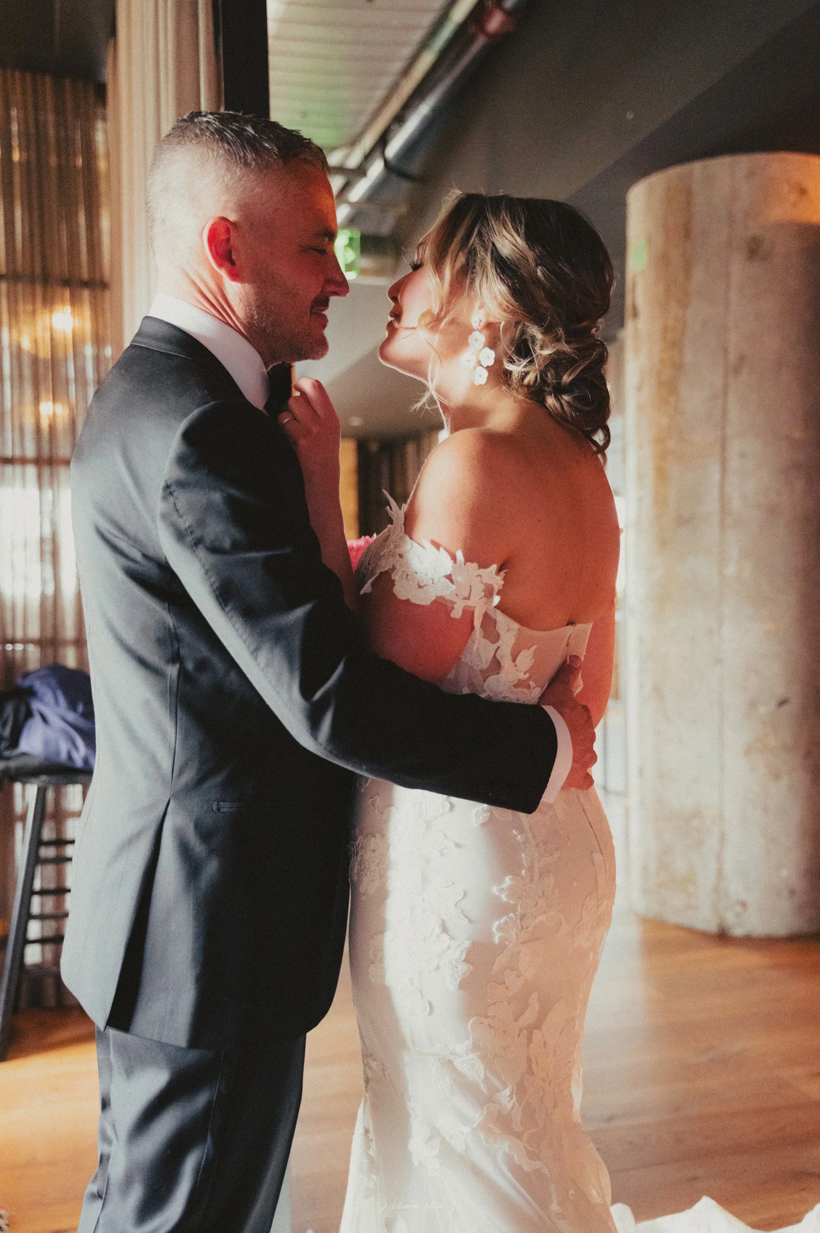 A bride and groom sharing a dance, looking into each other's eyes, indoors with warm lighting.