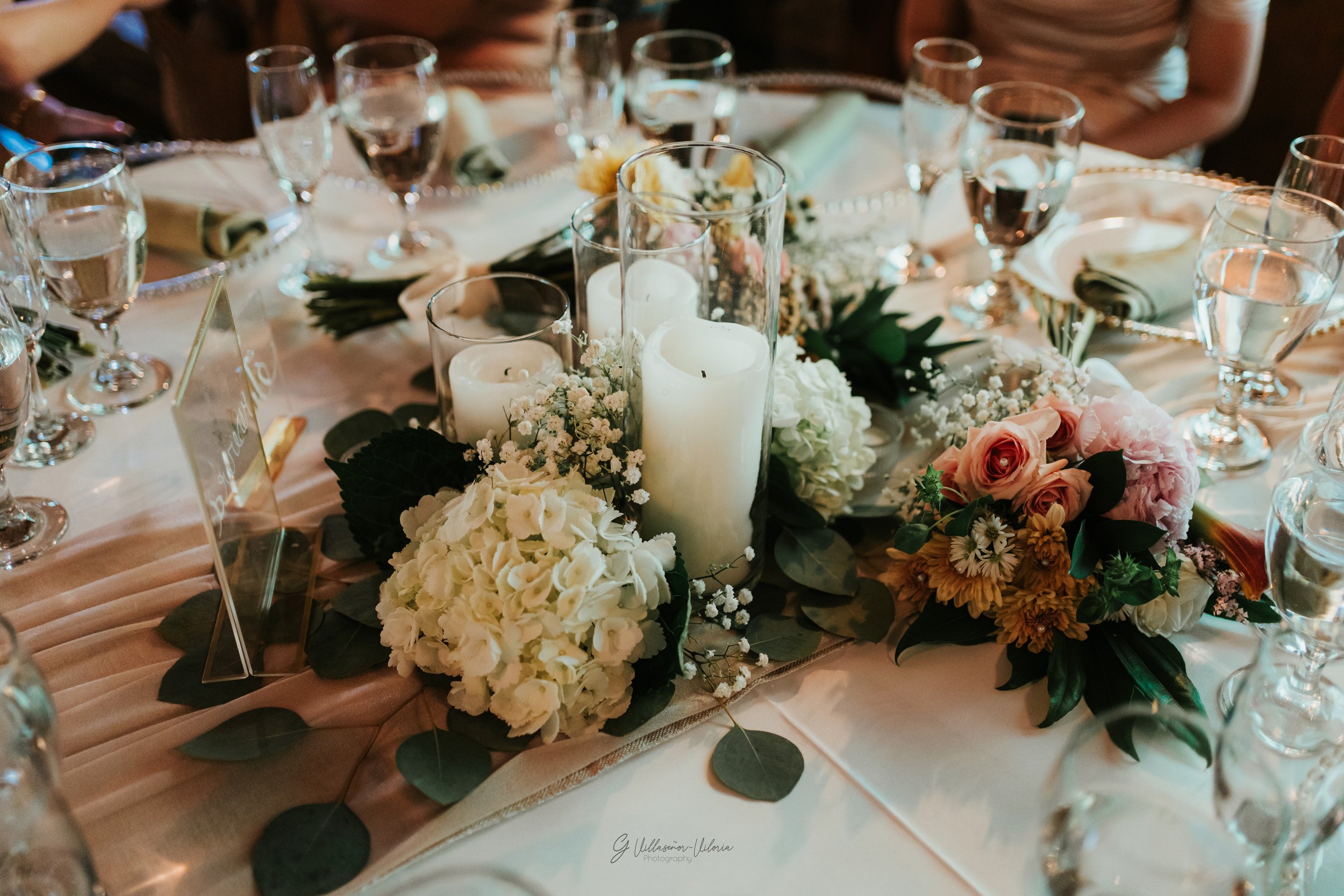 Table decorated with white and peach flowers, candles, and glassware for a formal event.
