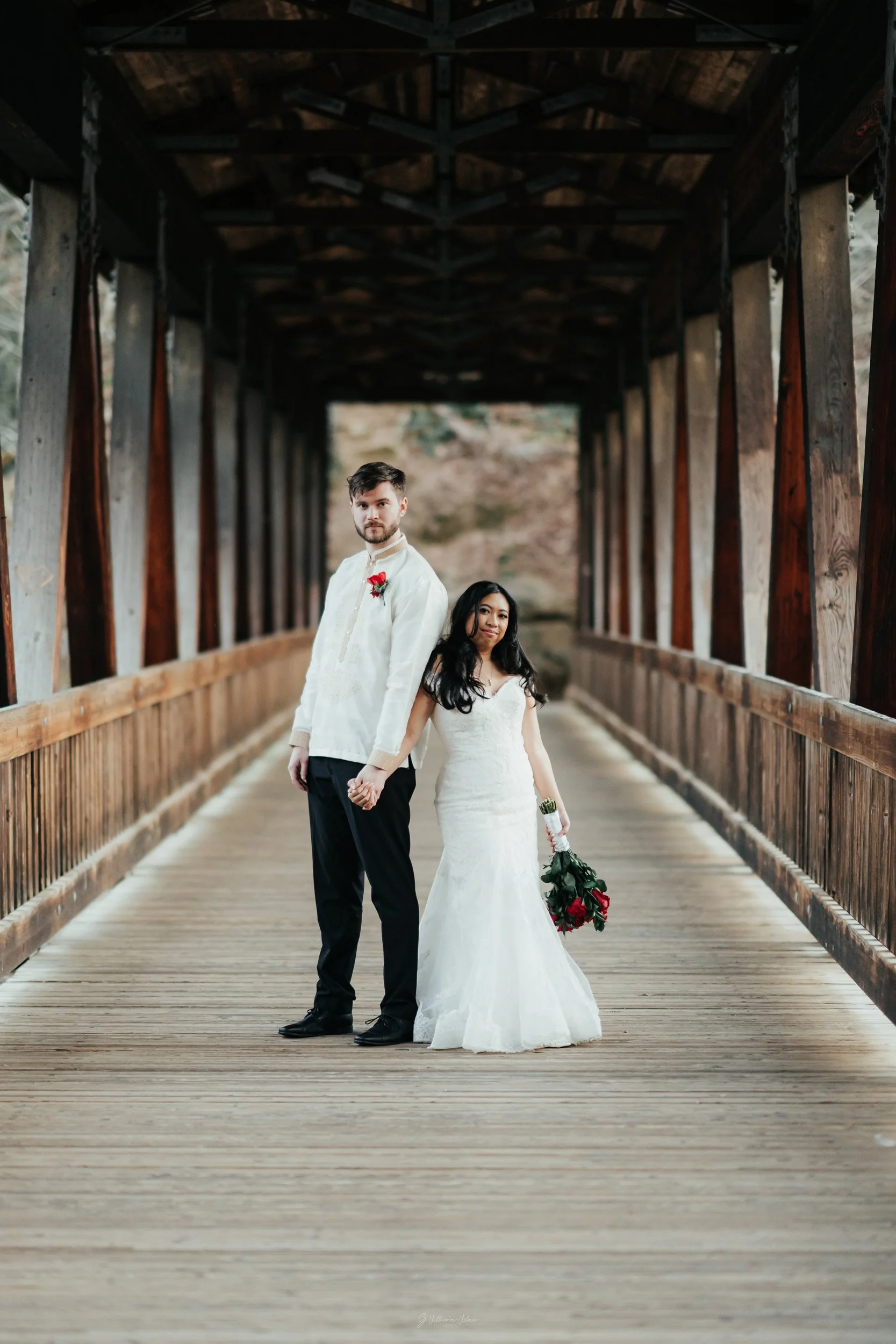 A bride and groom holding hands on a wooden covered bridge during their wedding photoshoot.