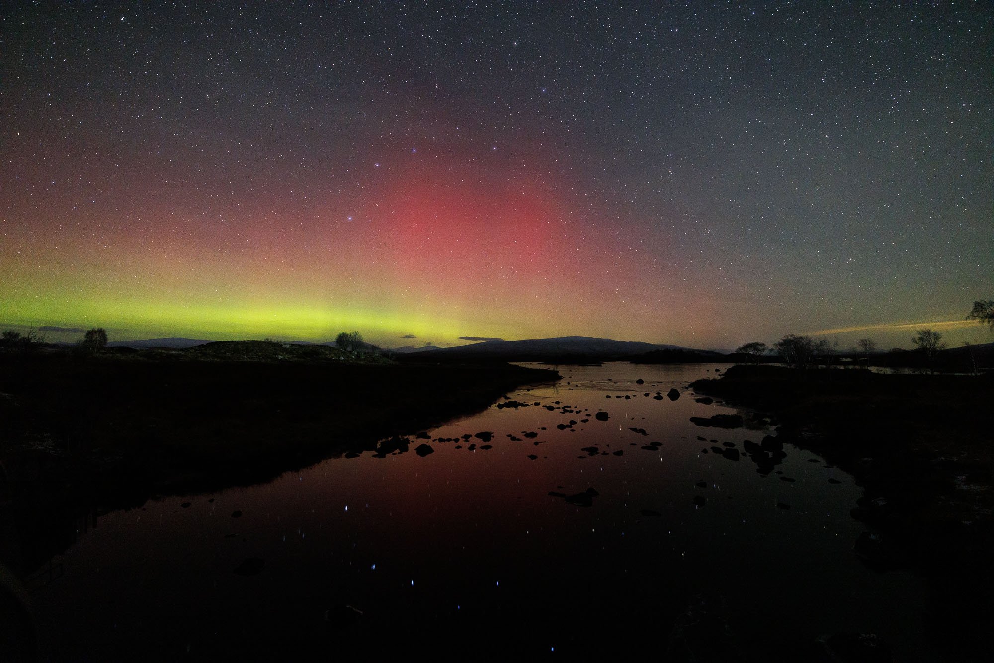 Glencoe, Scotland,  sky with colorful aurora borealis over a river and silhouette trees.
