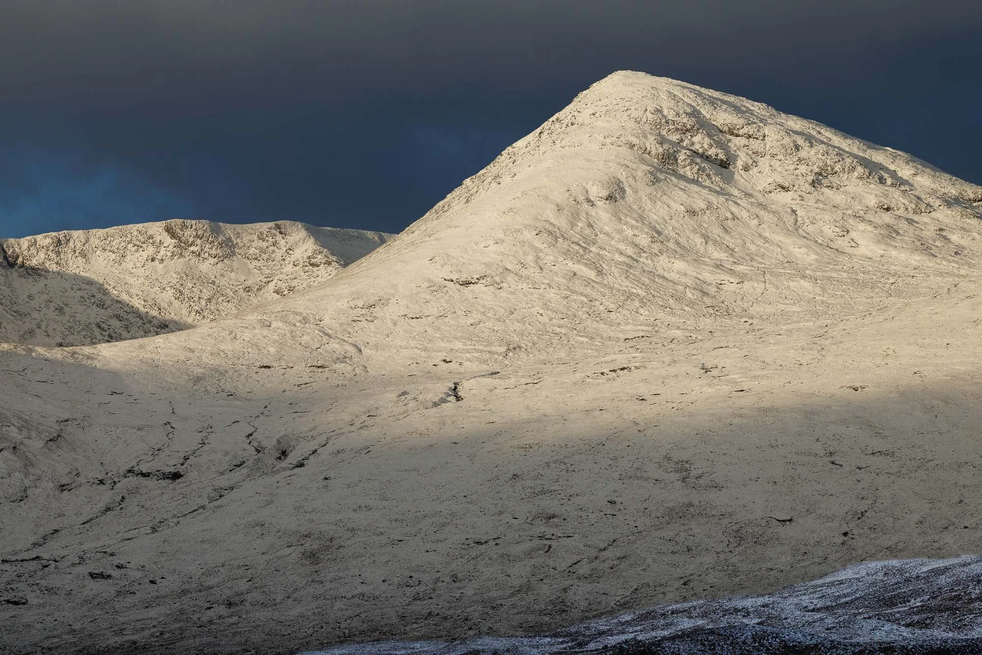 Glencoe, Scotland, snow-covered mountain with dark clouds in the sky.