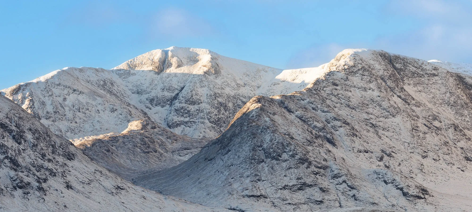 Glencoe, Scotland, snow-covered mountain range under a clear blue sky.