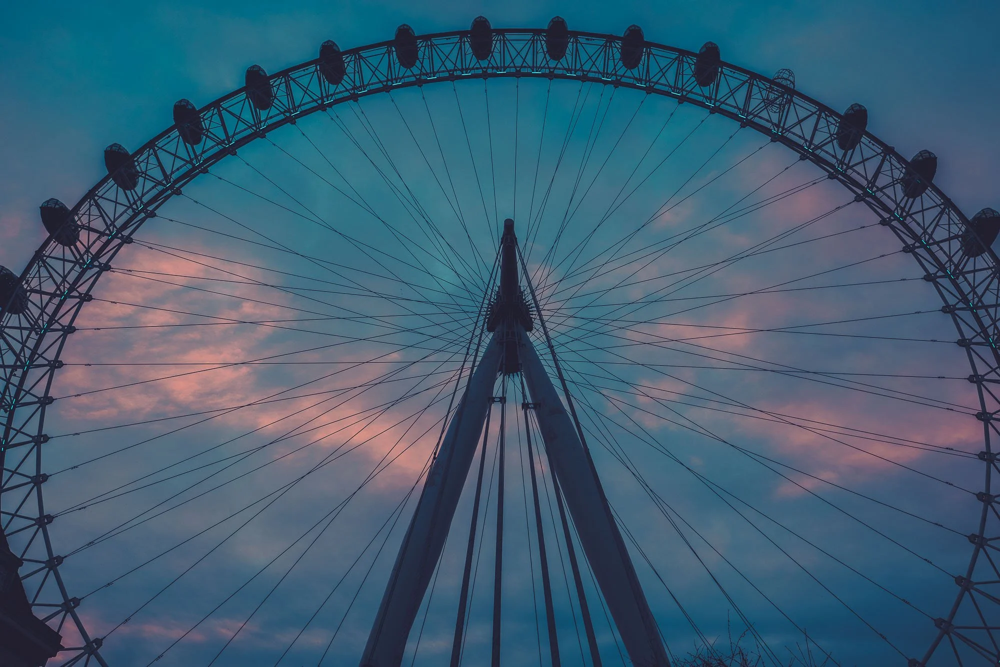 View of a large Ferris wheel against a pink and blue sunset sky, taken from directly below.