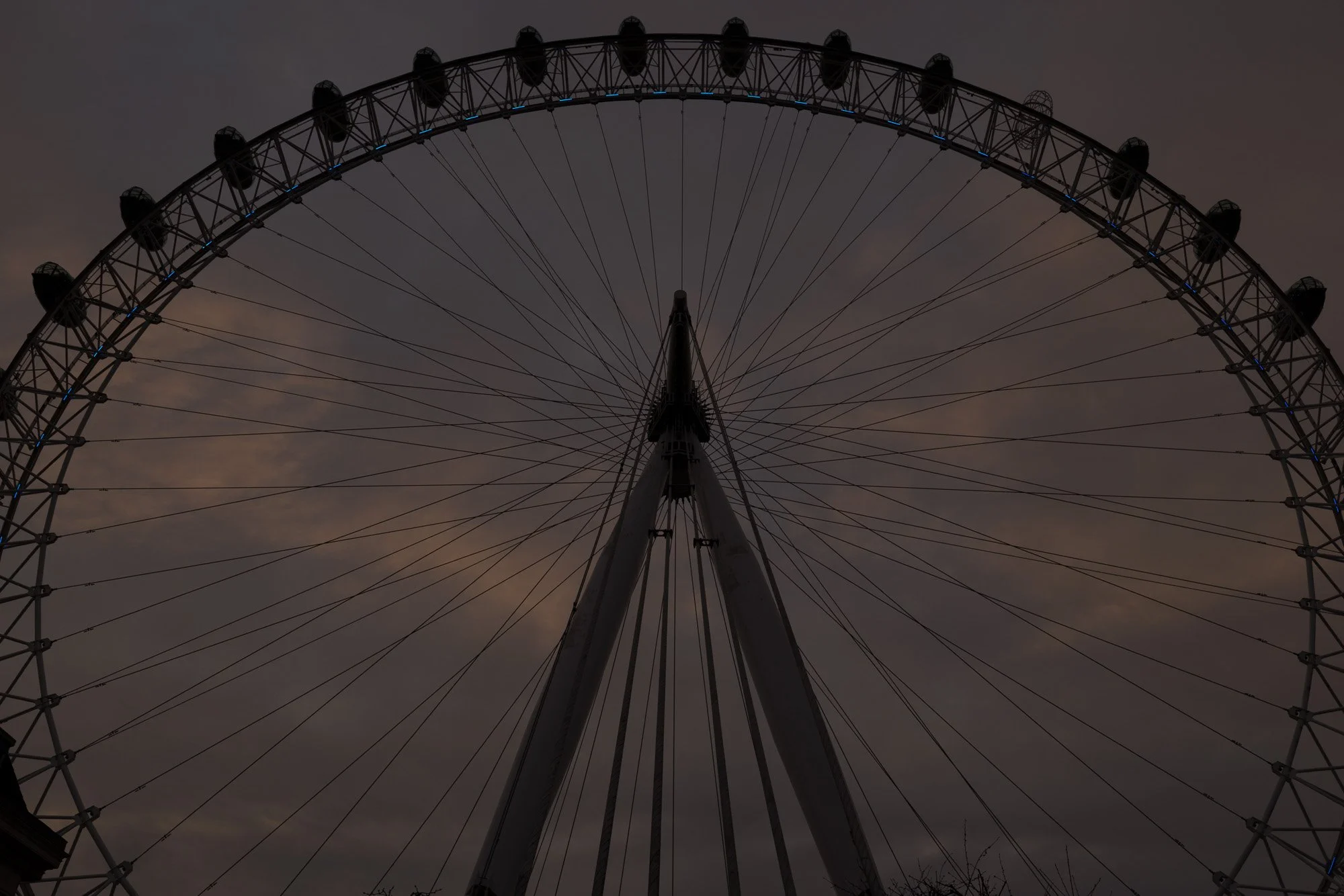 London Eye silhouetted against a cloudy, dusk sky with the lights on.