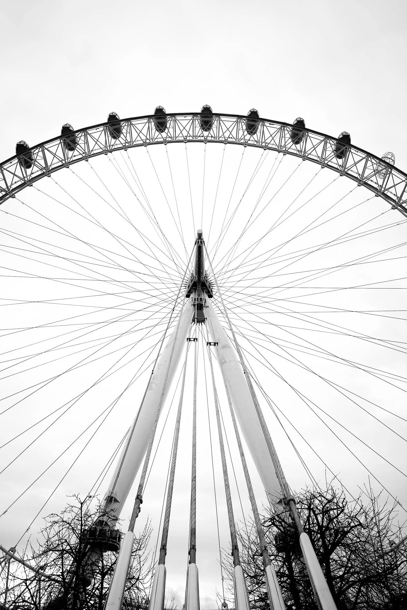 Black and white photo of a large Ferris wheel seen from below, with empty cabins and the wheel's support structure against a cloudy sky.
