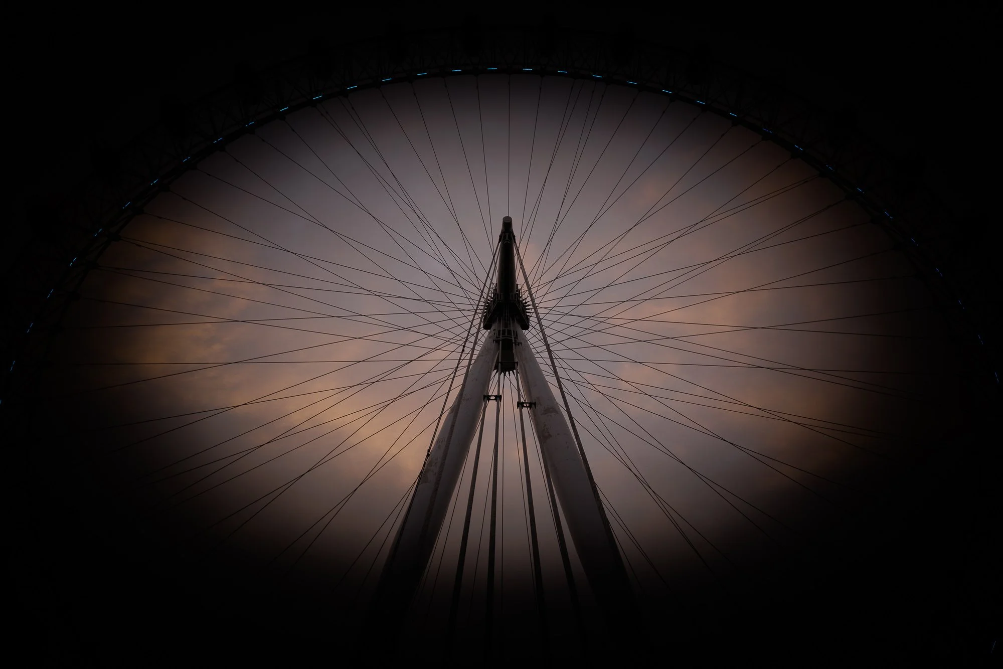 Looking up at a London Eye at dusk with a cloudy sky in the background.
