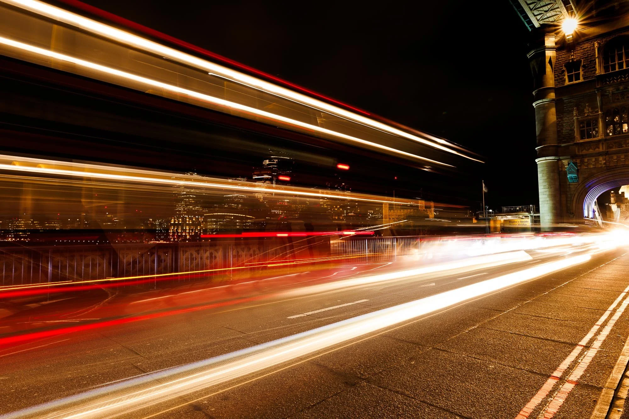 Nighttime city street with blurred light trails from moving cars, and illuminated buildings in the background.