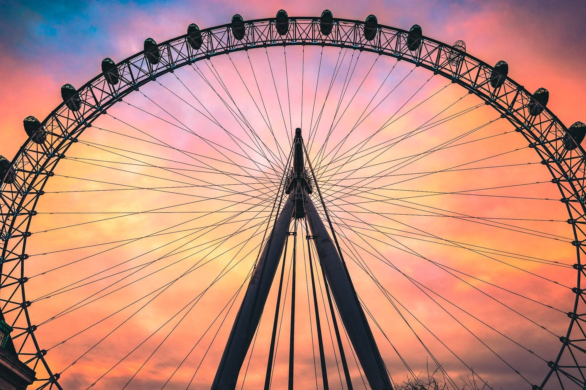 A large Ferris wheel against a colorful sunset sky with shades of pink, orange, and blue.
