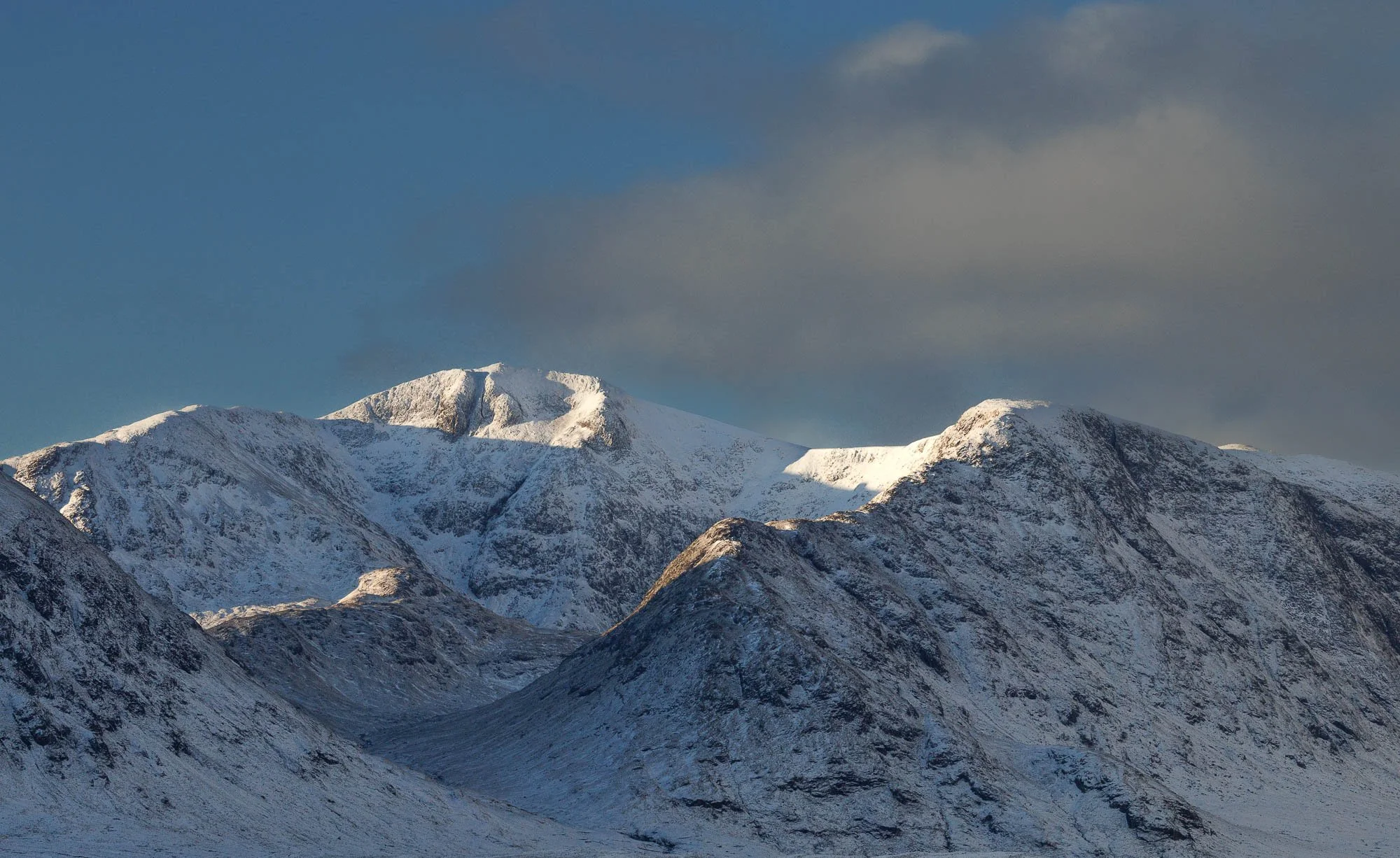 Glencoe, Scotland, snow-covered mountain range under a cloudy sky.