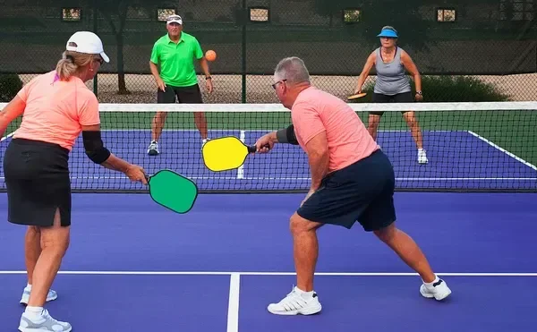 Four people playing pickleball on a blue outdoor court, with two near the net holding paddles and two in the background.
