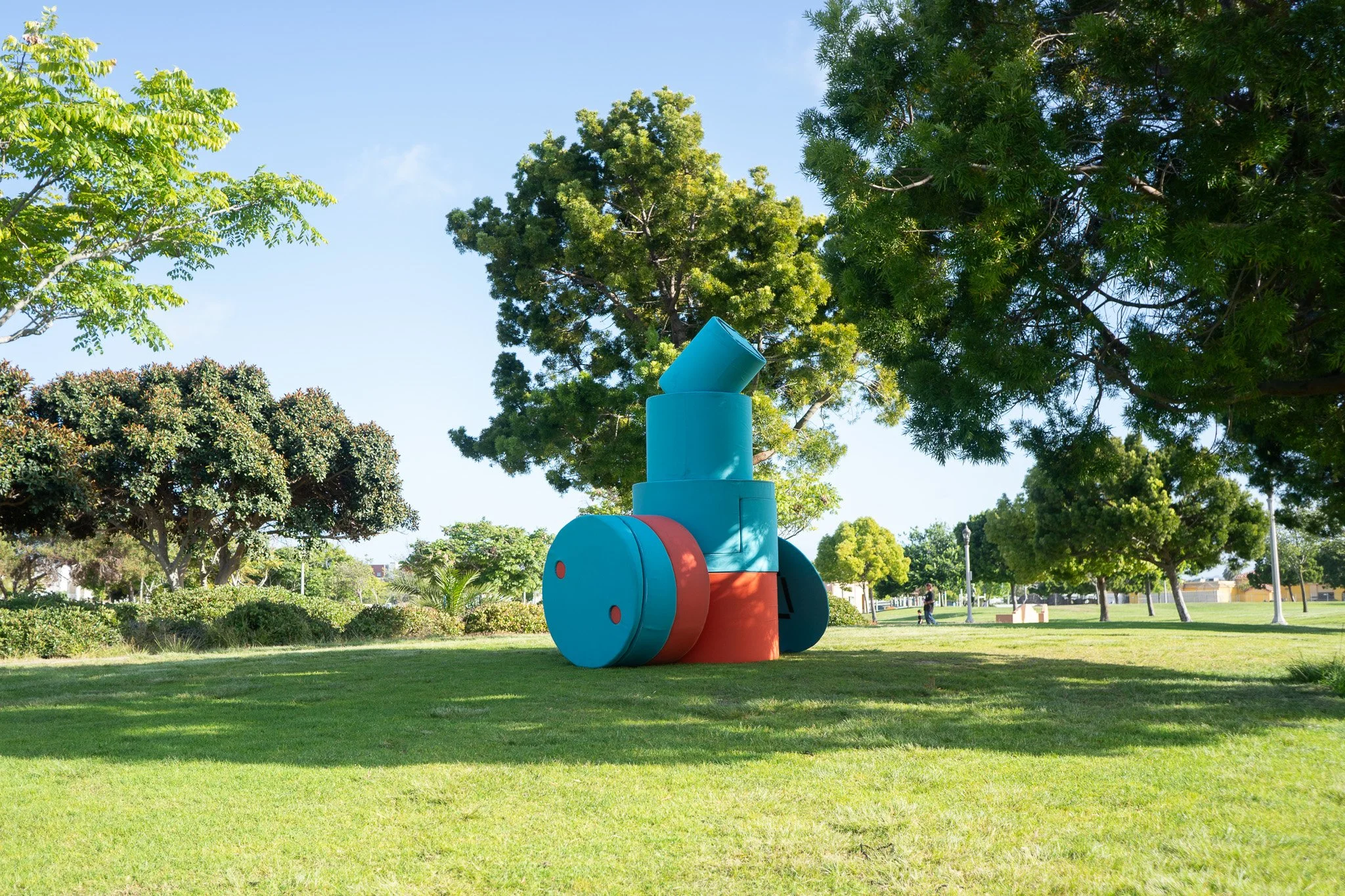 Colorful abstract sculpture in a park, surrounded by green grass and trees, under a clear blue sky.