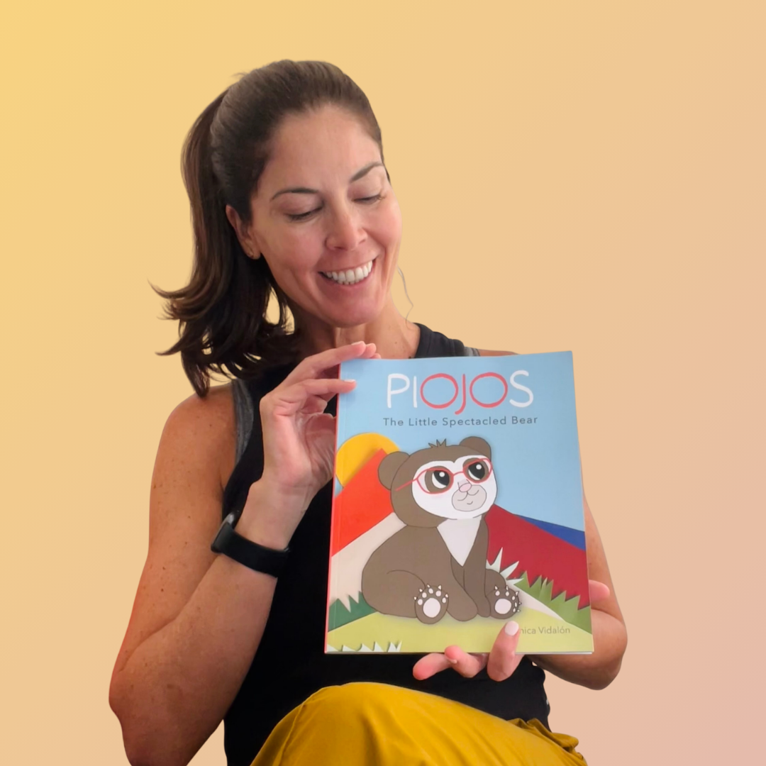Author smiling and holding a colorful children's book titled 'PIOJOS: The Little Spectacled Bear', featuring a sweet spectacled bear wearing glasses on the cover.
