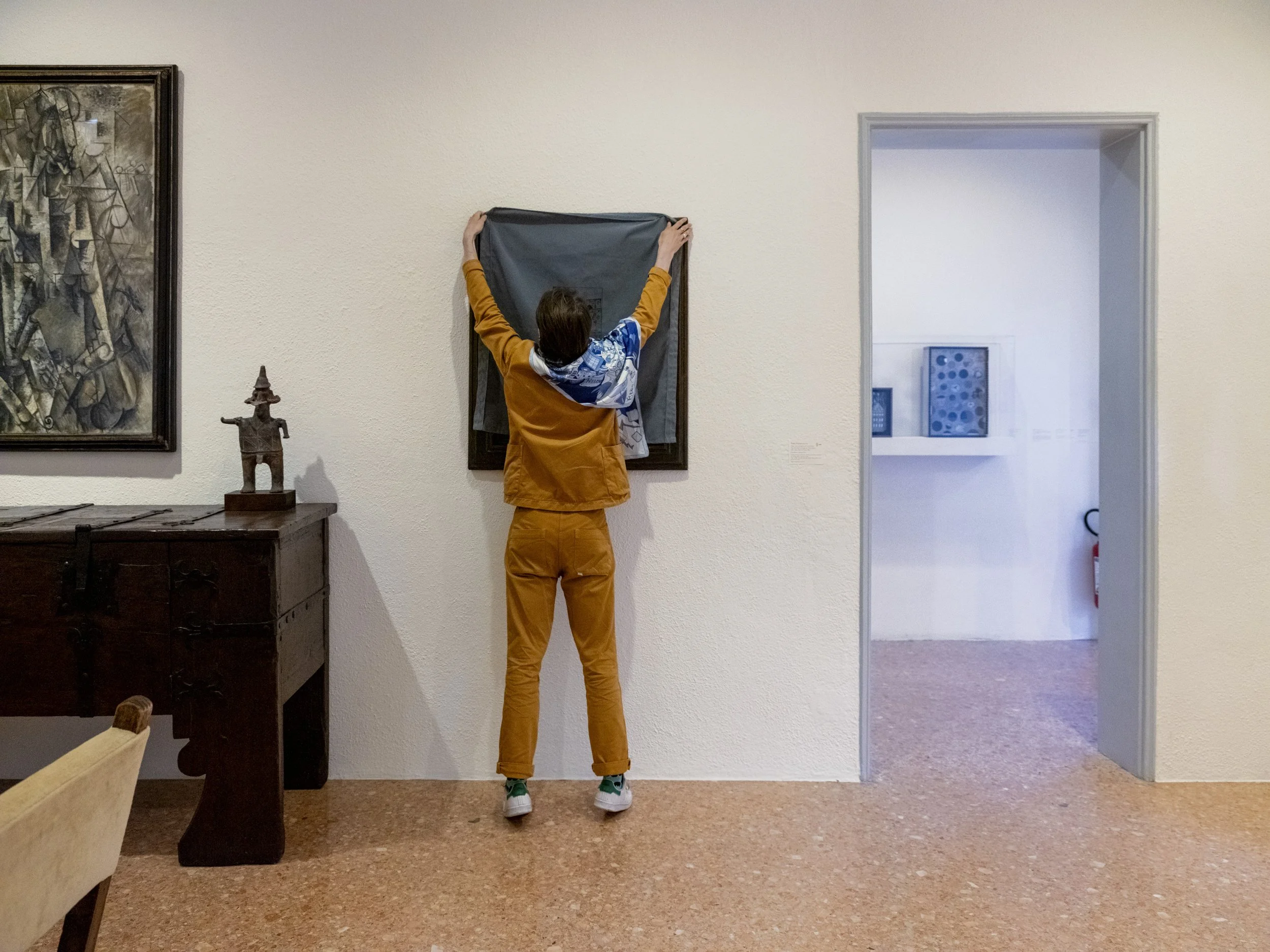 A person in an orange outfit hanging a gray cloth on the wall in an art gallery.