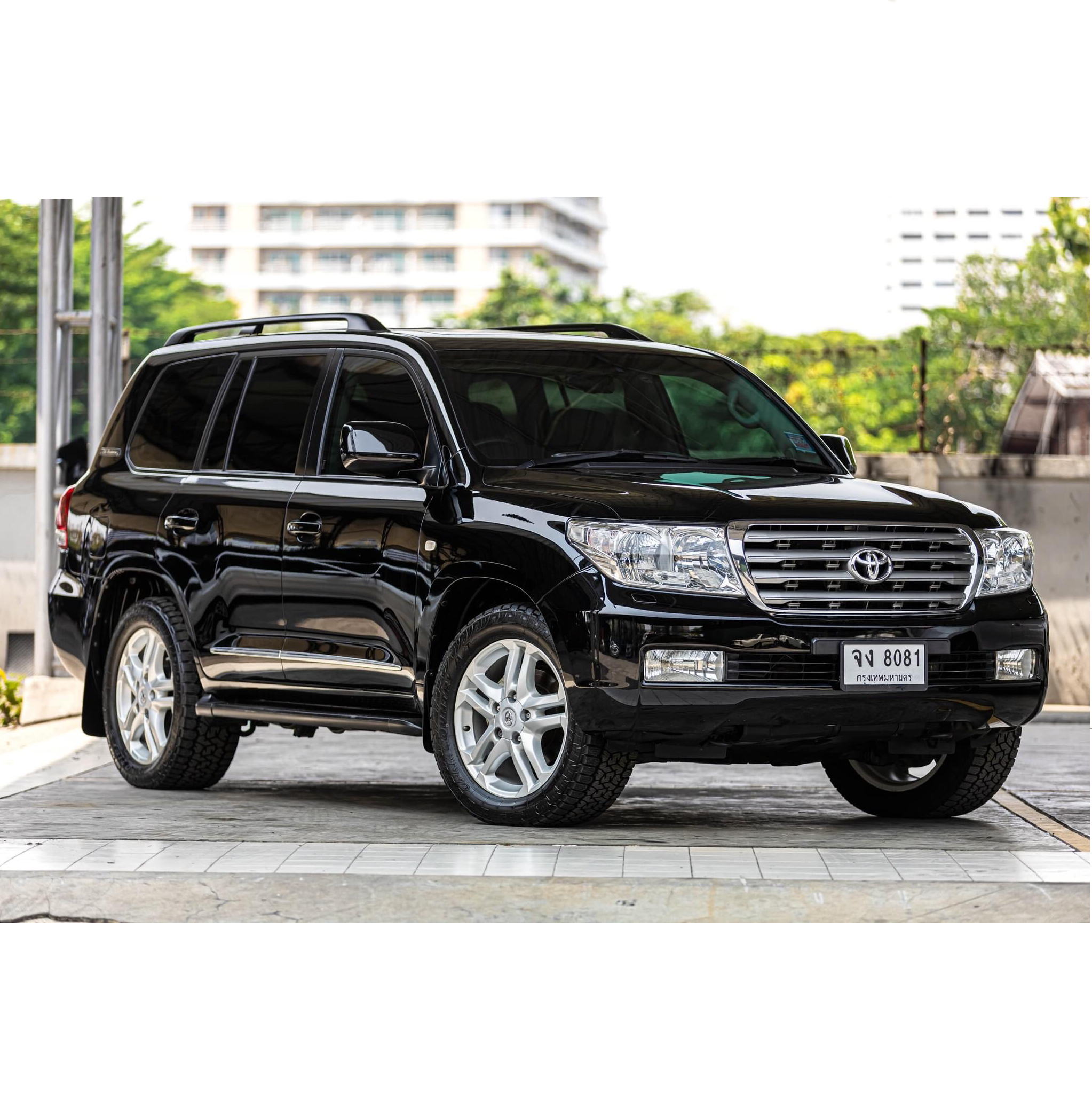Black Toyota SUV parked in an outdoor parking lot with greenery and tall buildings in the background.