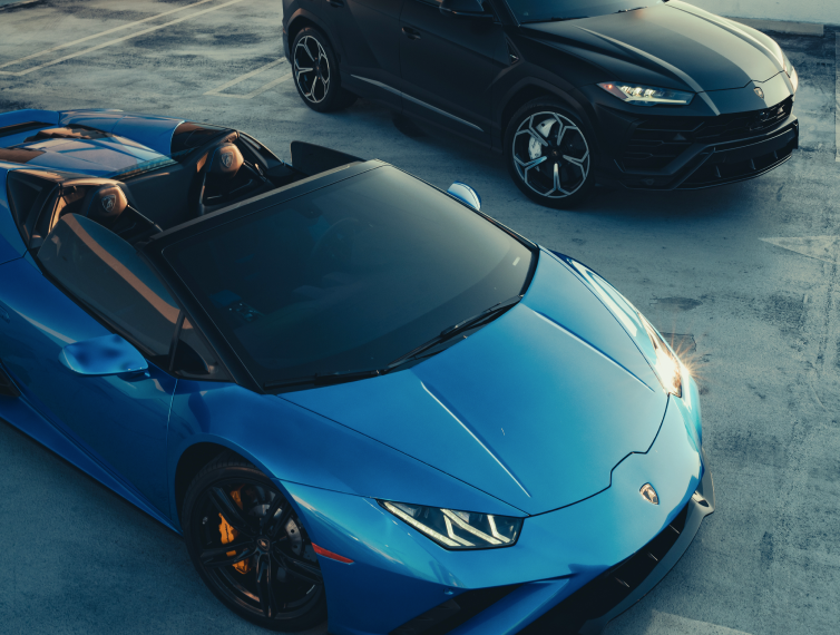 A blue Lamborghini convertible and a black Lamborghini coupe parked in an outdoor lot.