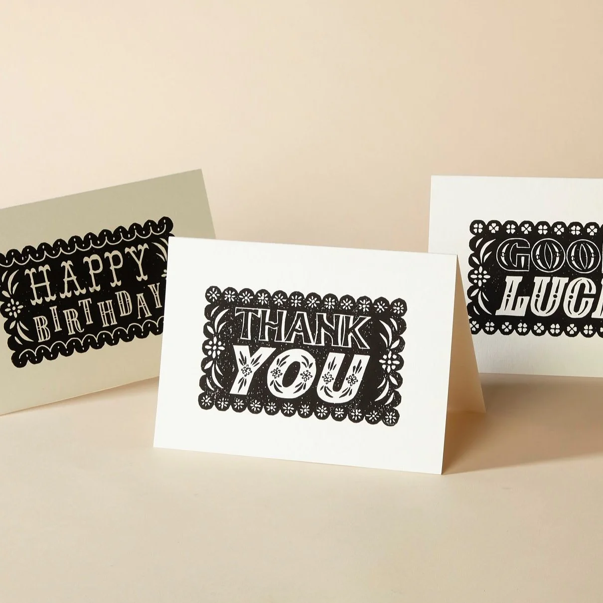 Three greeting cards with ornate black text: 'Happy Birthday,' 'Thank You,' and 'Good Luck.' The cards are displayed on a light beige background.