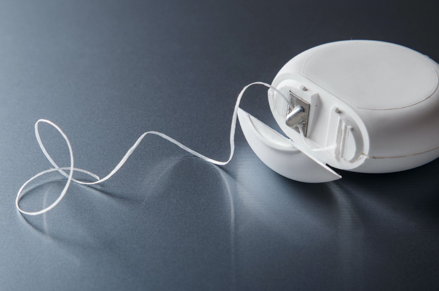 A tape dispenser with a long, white, loose tape roll on a dark, slightly textured surface.
