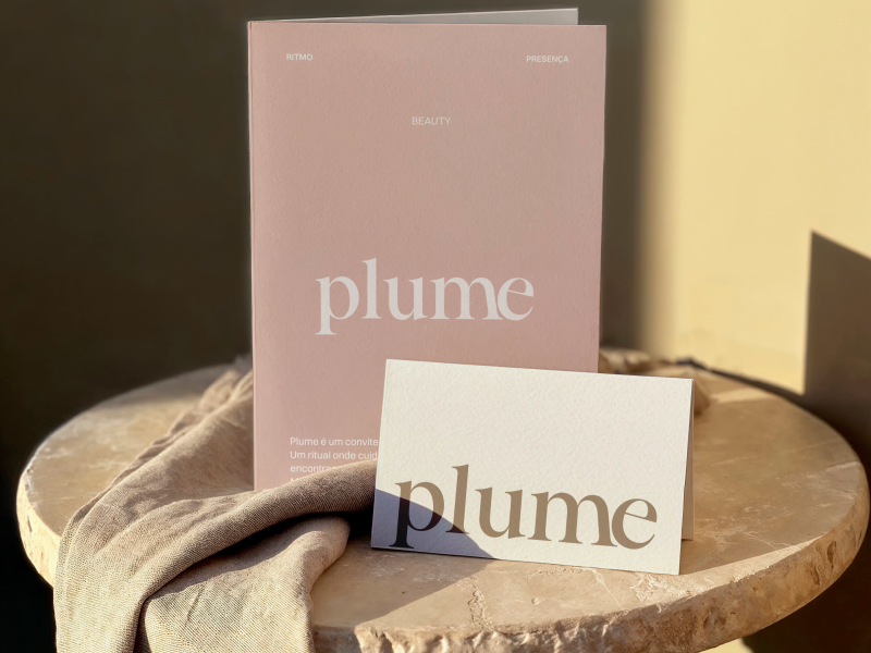 Plume Beauty brand identity mockup featuring a blush pink editorial booklet and ivory card with elegant serif wordmarks, styled with natural linen on a stone table in warm sunlight.