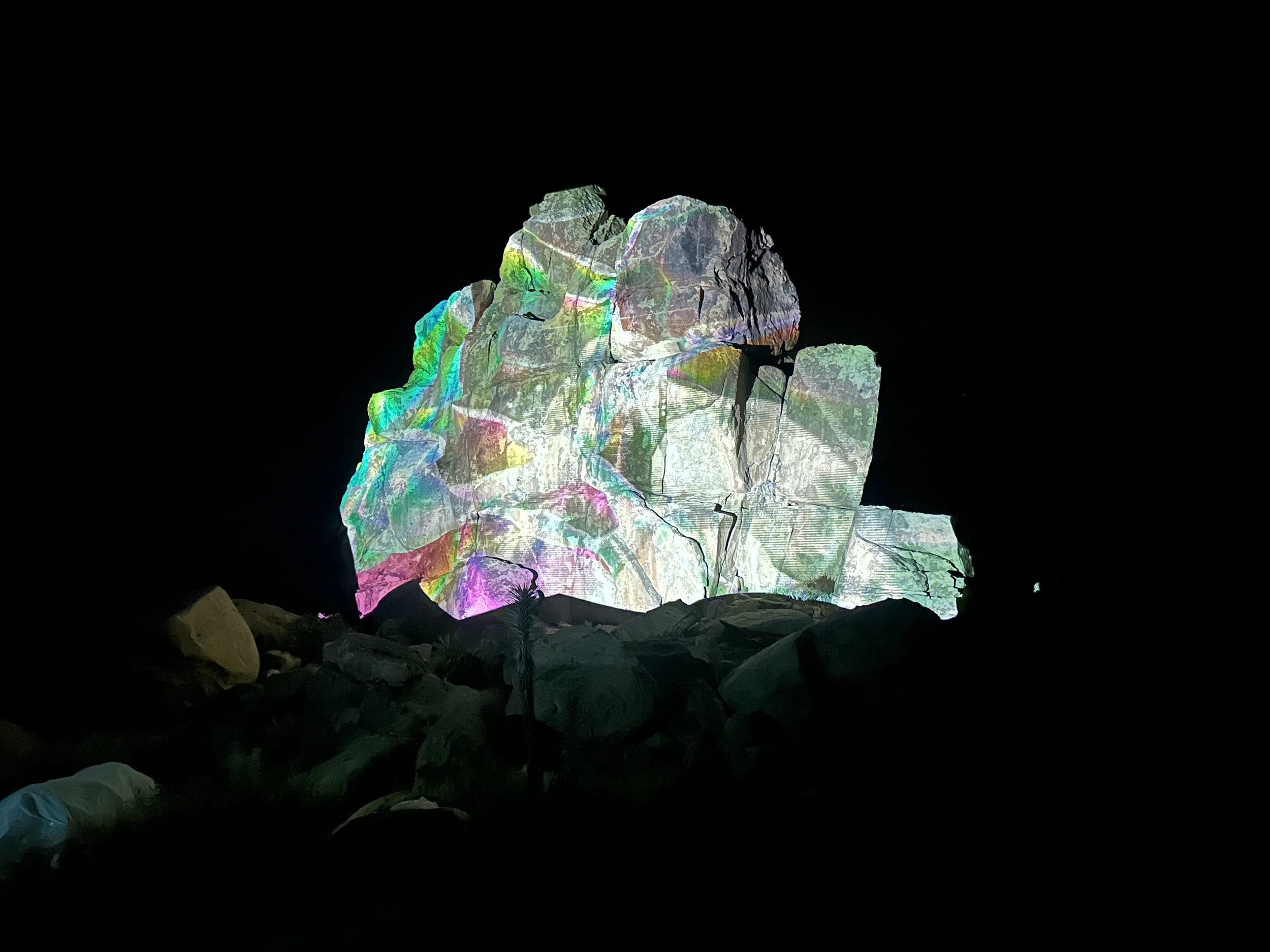 Projection mapping installation illuminating a rock formation in Joshua Tree, California with vibrant abstract visuals.