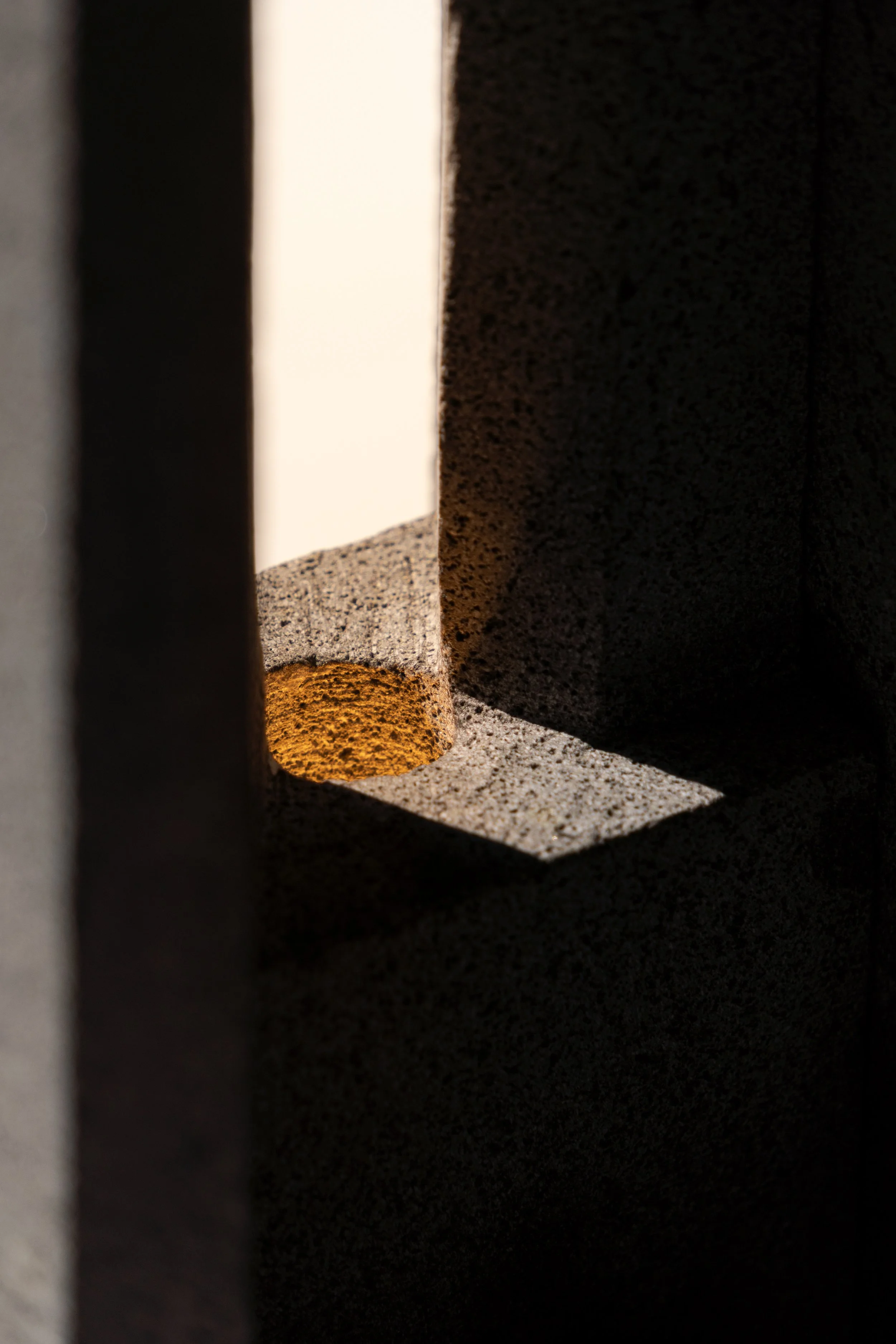 Vista a través de un espacio estrecho en una estructura de piedra, con sombra y luz resaltando la textura de la piedra