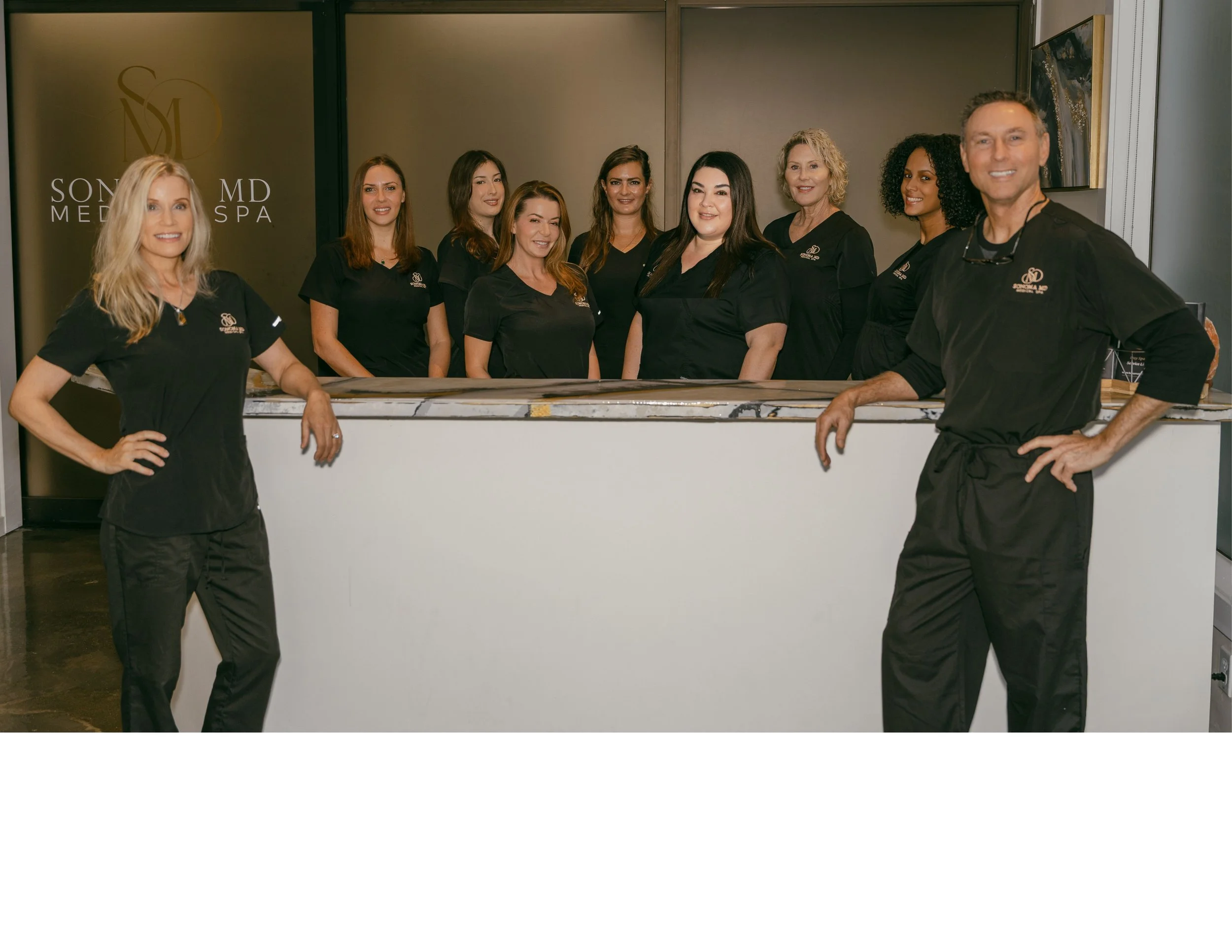 Group of nine staff members wearing black uniforms at the reception desk of Soma MD Med Spa.