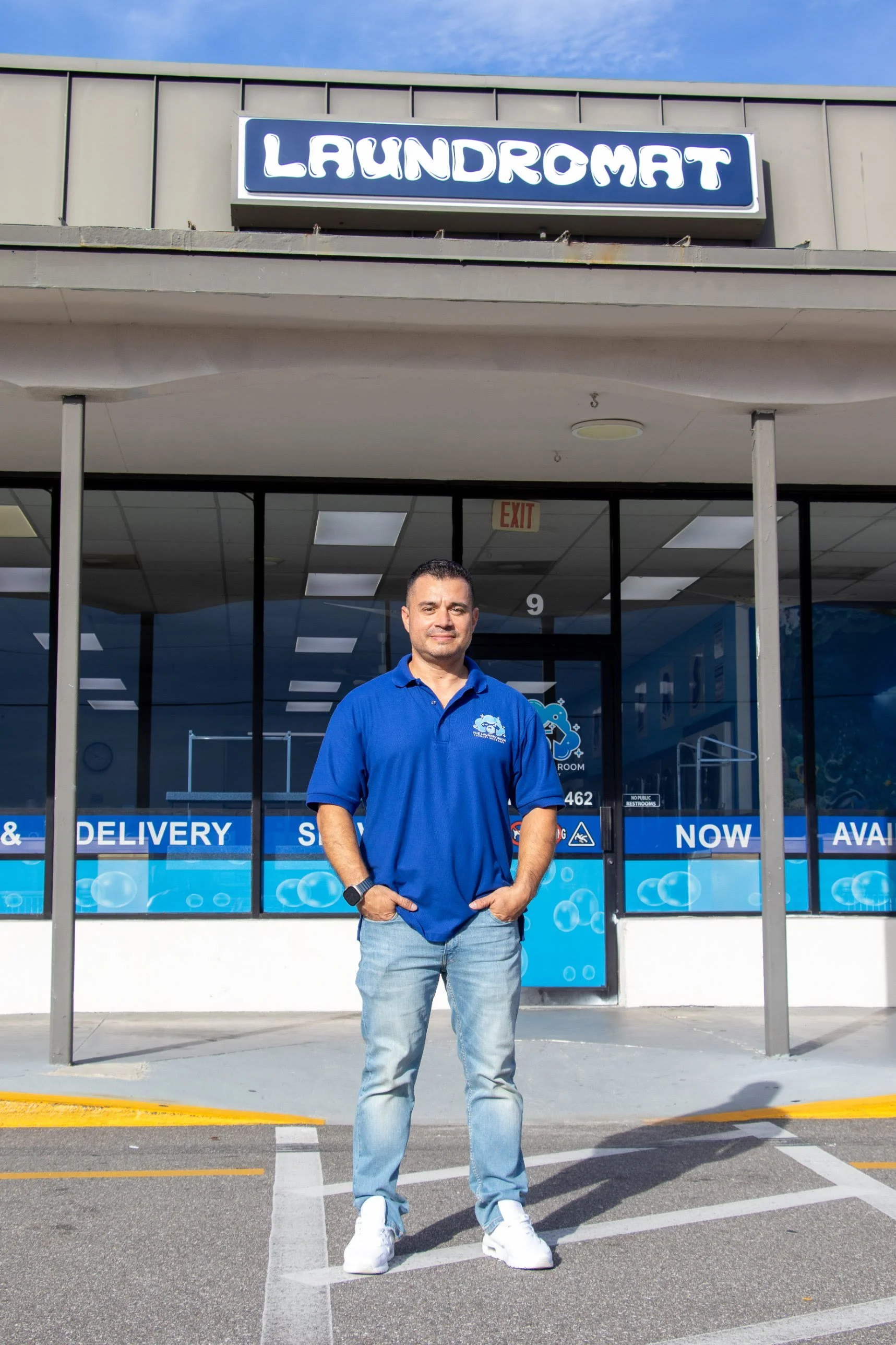 Leonard, owner of The Laundry Room, standing outside his laundromat in a branded polo