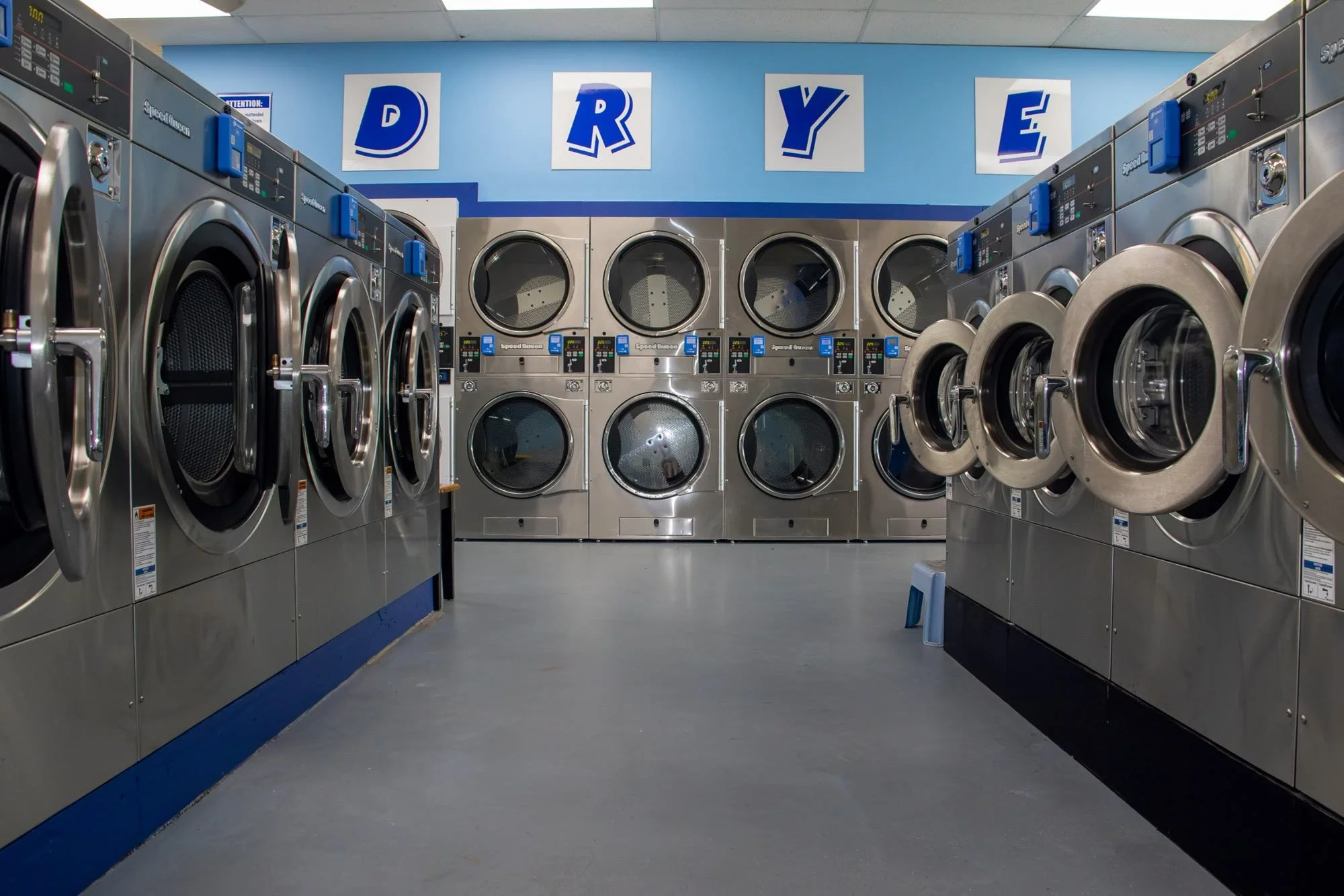 Rows of stainless steel washers and dryers inside The Laundry Room laundromat