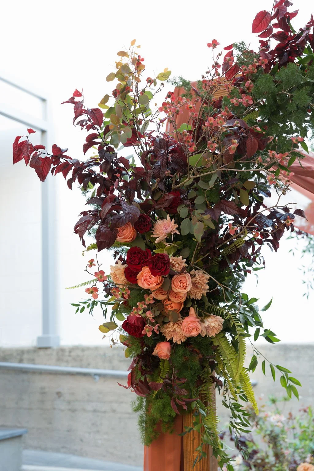 A large floral arrangement with pink, peach, and red roses, surrounded by greenery and attached to a wooden structure, likely for a celebration or event.