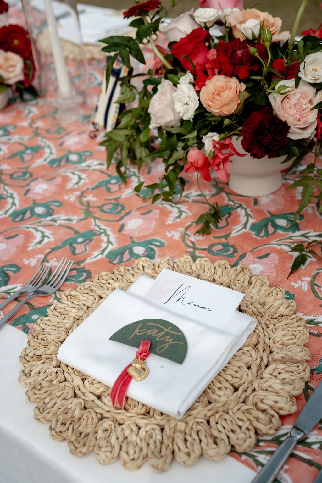A beautifully set table with a floral centerpiece, a menu card, and silverware on a patterned tablecloth.