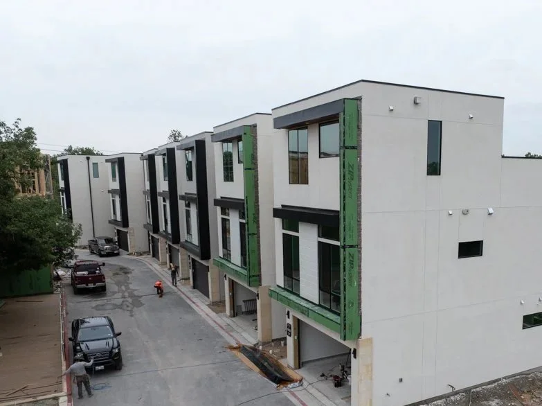 Modern multi-story residential buildings under construction with parked cars nearby.