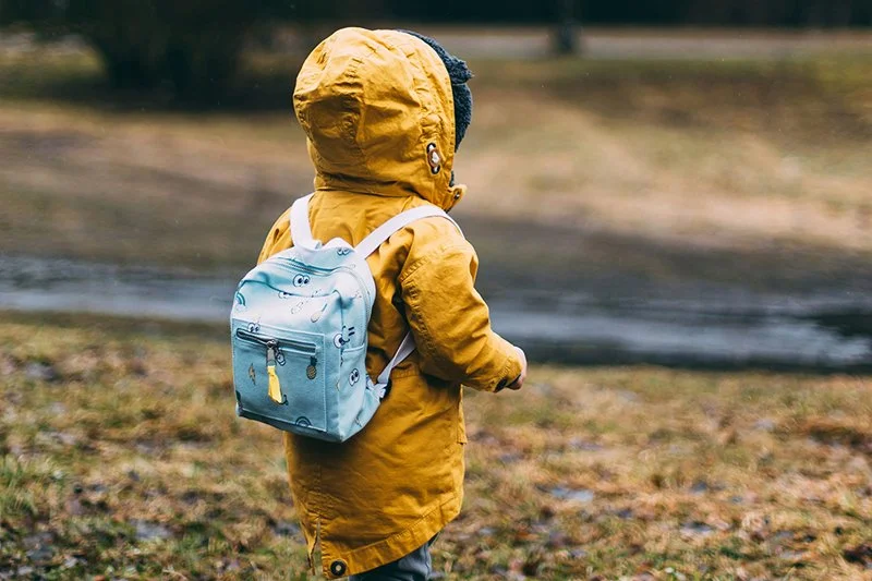 A child wearing a yellow rain coat and a blue backpack.