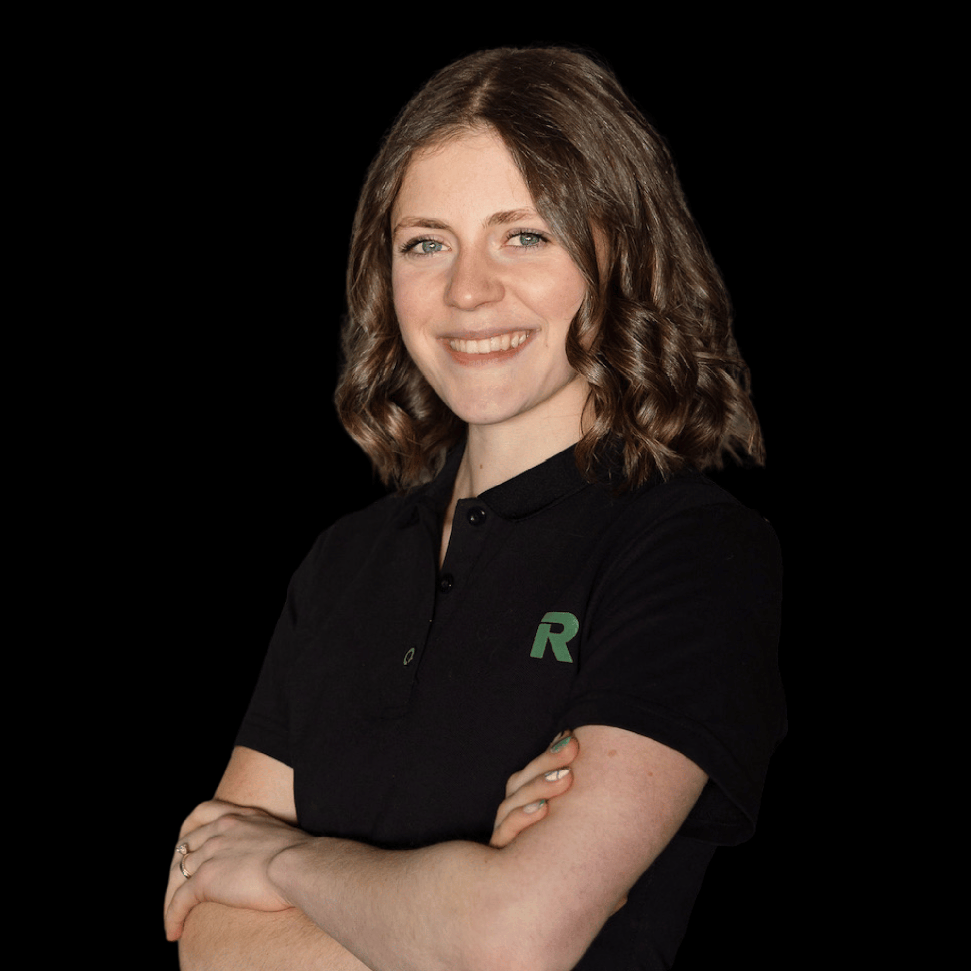 A young woman with shoulder-length brown curly hair, smiling, wearing a black polo shirt with a green 'R' logo on the chest, standing against a black background.