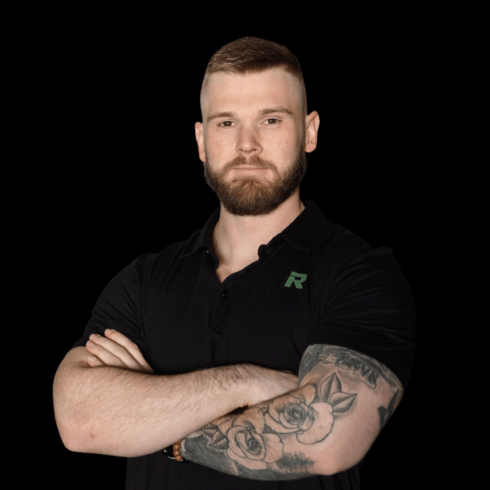 A man with a beard and short hair standing with arms crossed, wearing a black polo shirt with a green logo, against a black background.
