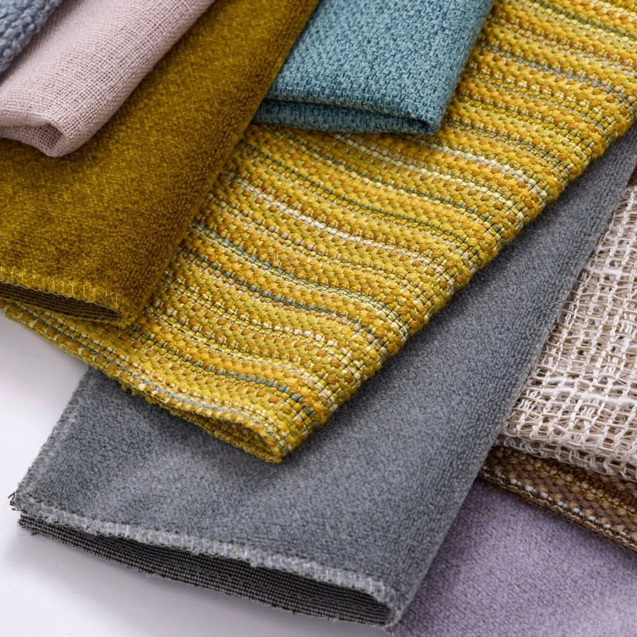 Stacked assorted fabric swatches in muted colors, including pink, yellow, blue, gray, woven, knit, and textured patterns.