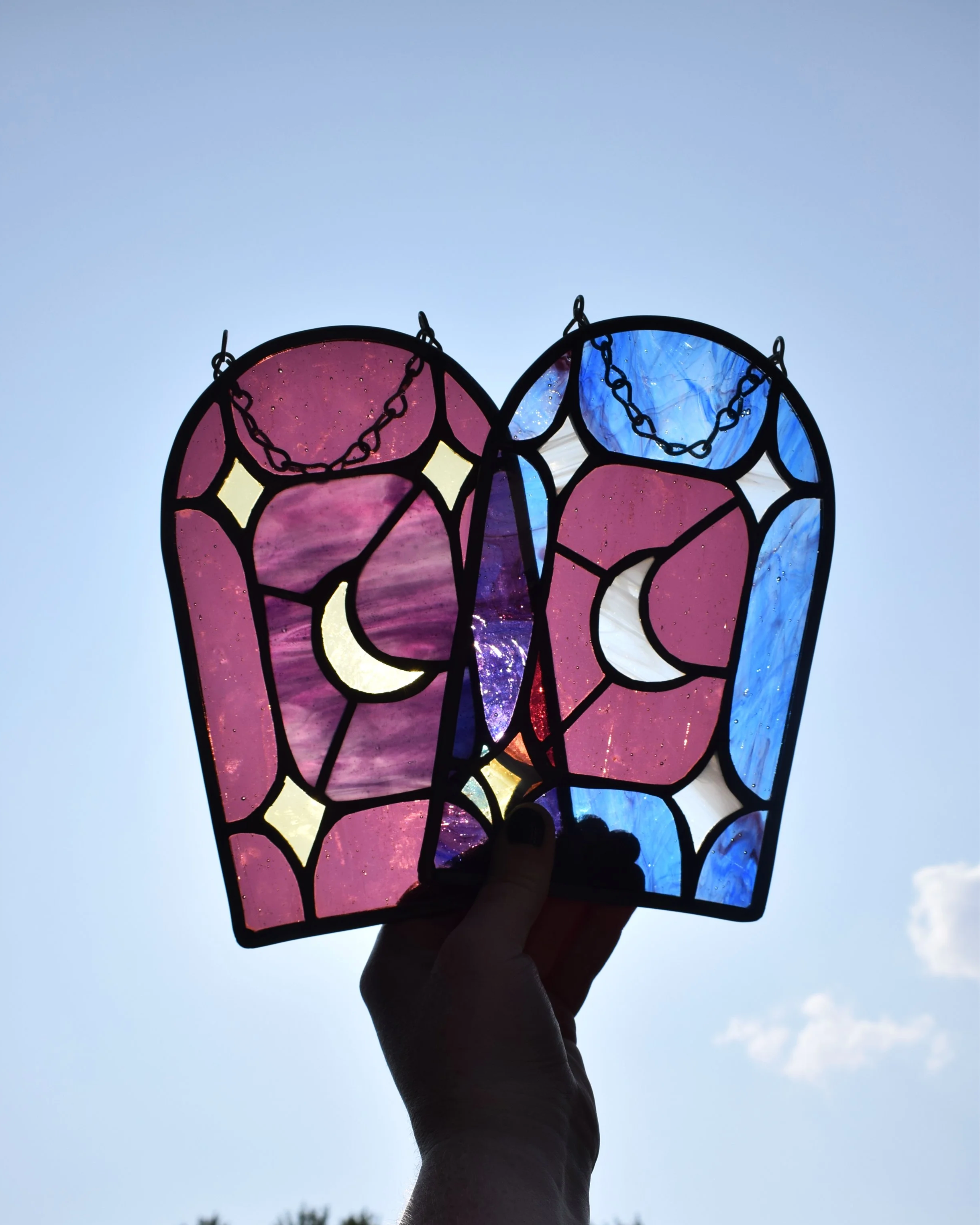 Colorful stained glass artwork with flowers, leaves, and a candle, being held up against a plain background.