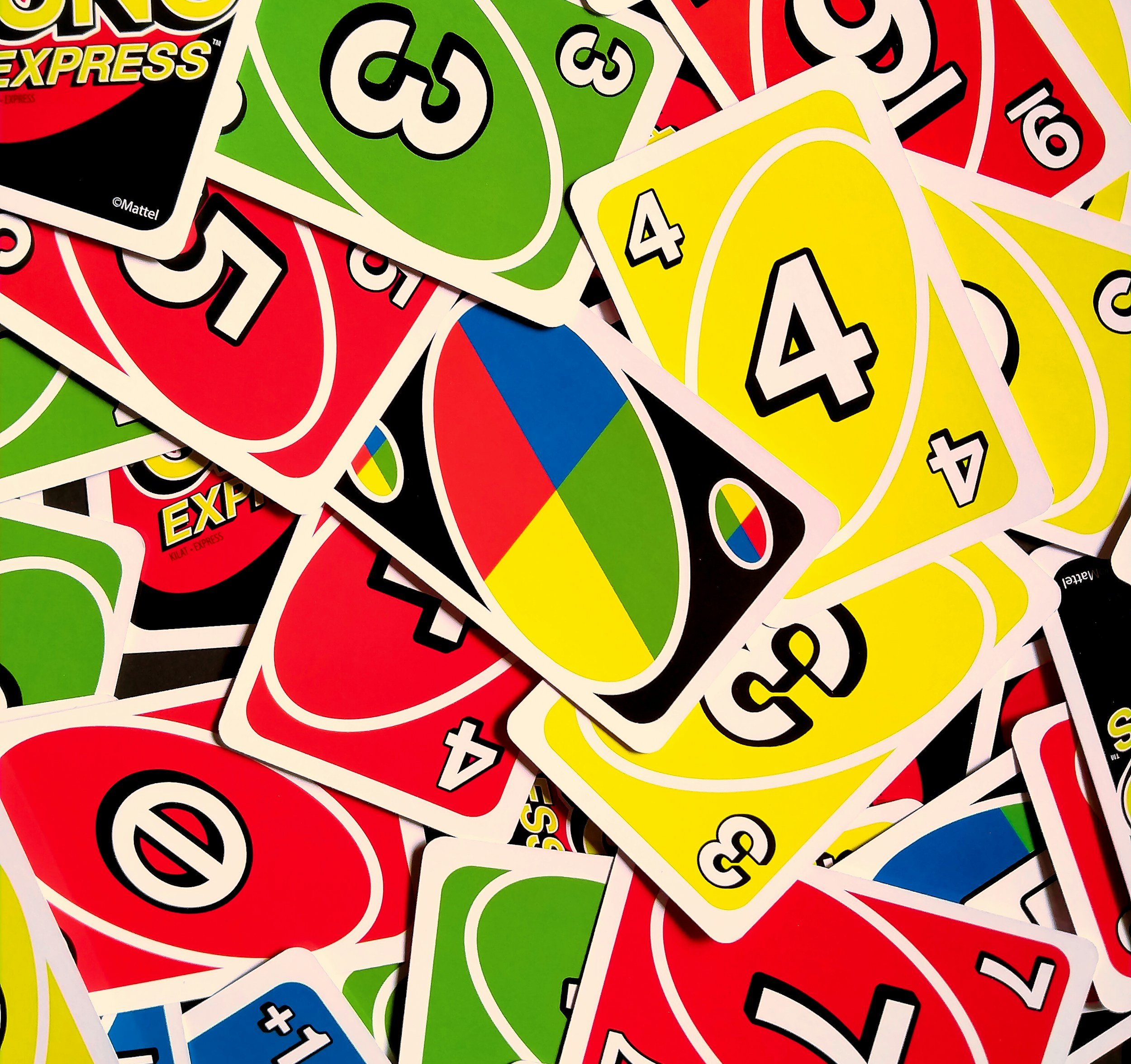 A pile of UNO cards with numbers and colors, including yellow 4s, red 0s, green 3s, and blue 2s, along with a spinner card with red, yellow, green, and blue segments.