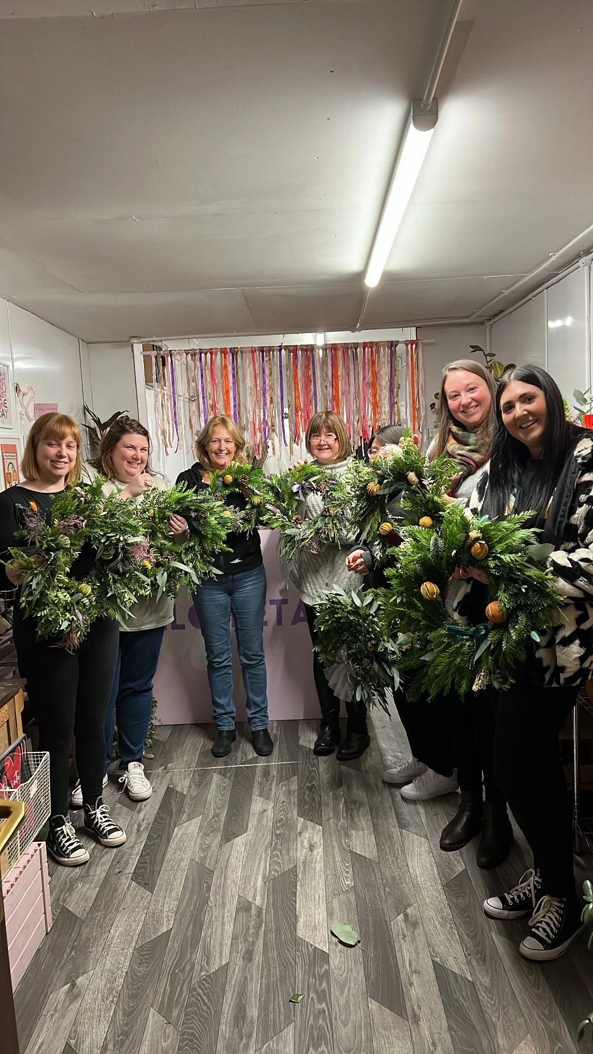 A group of women holding floral wreaths in a room decorated with streamers and posters.