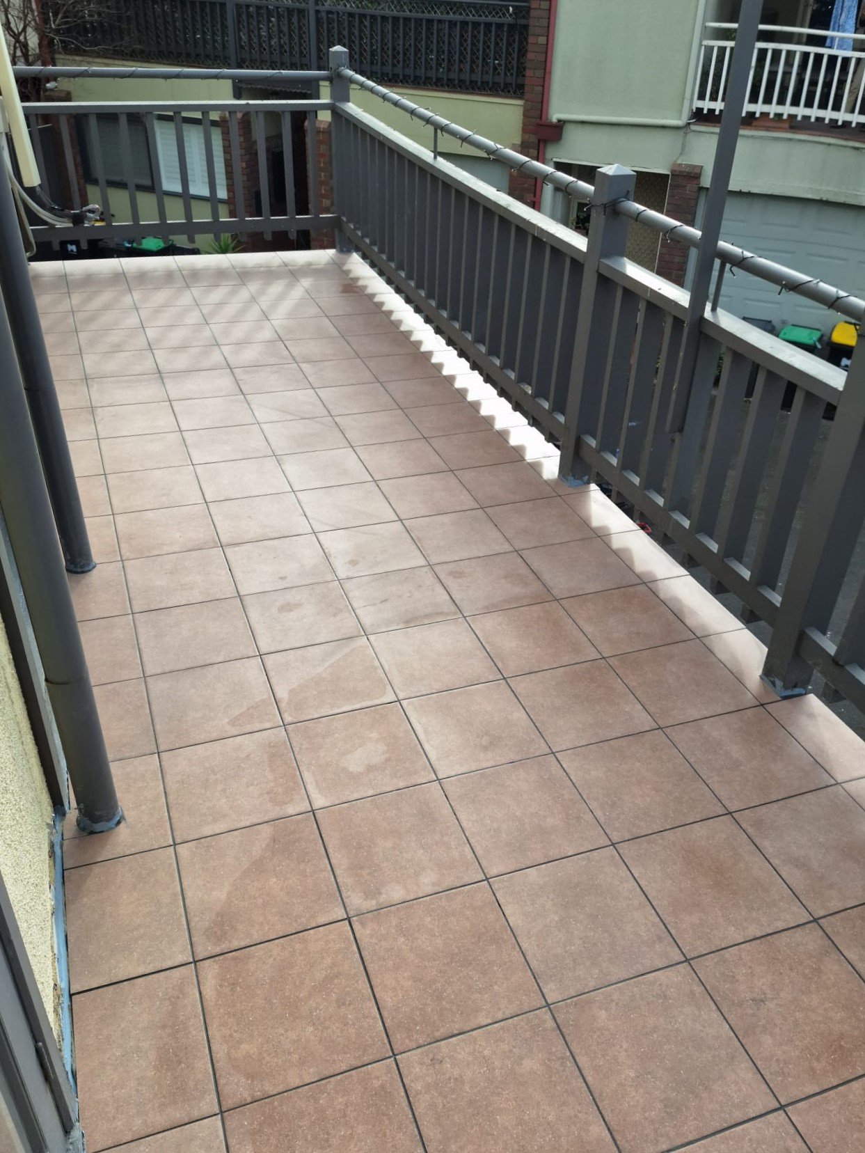 Outdoor balcony with square terracotta-coloured tiles and a dark railing.