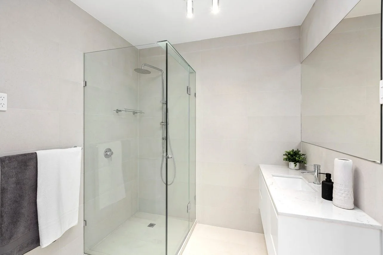 Tiled shower with a glass screen beside a bathroom vanity.