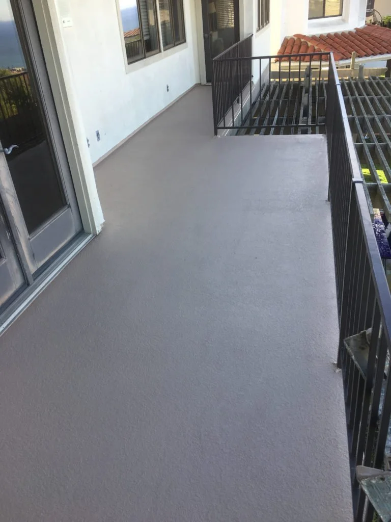 Balcony floor with a continuous grey waterproofing coating beside the exterior wall.