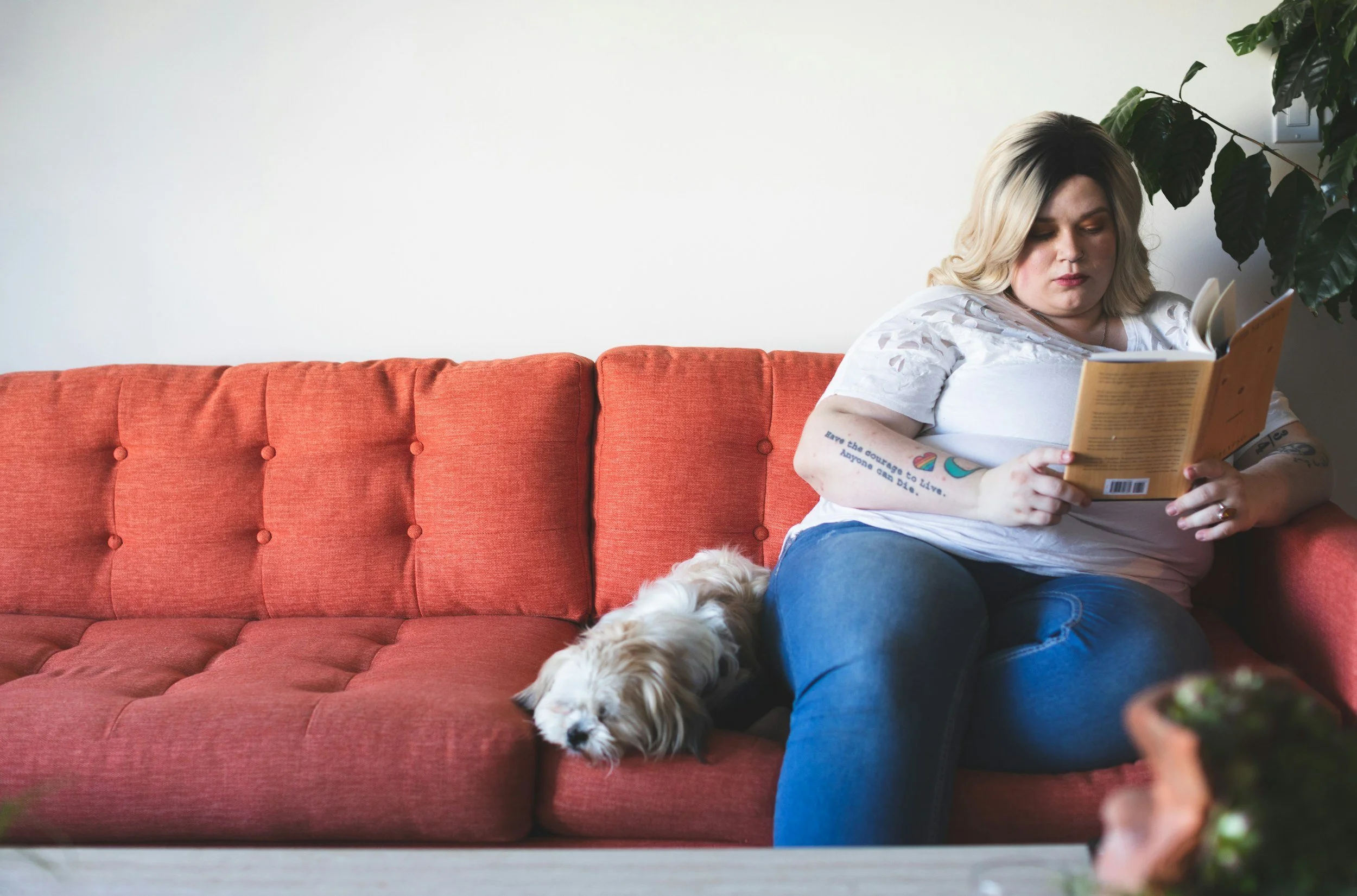 Woman reading a book about diet culture on a couch with her small dog