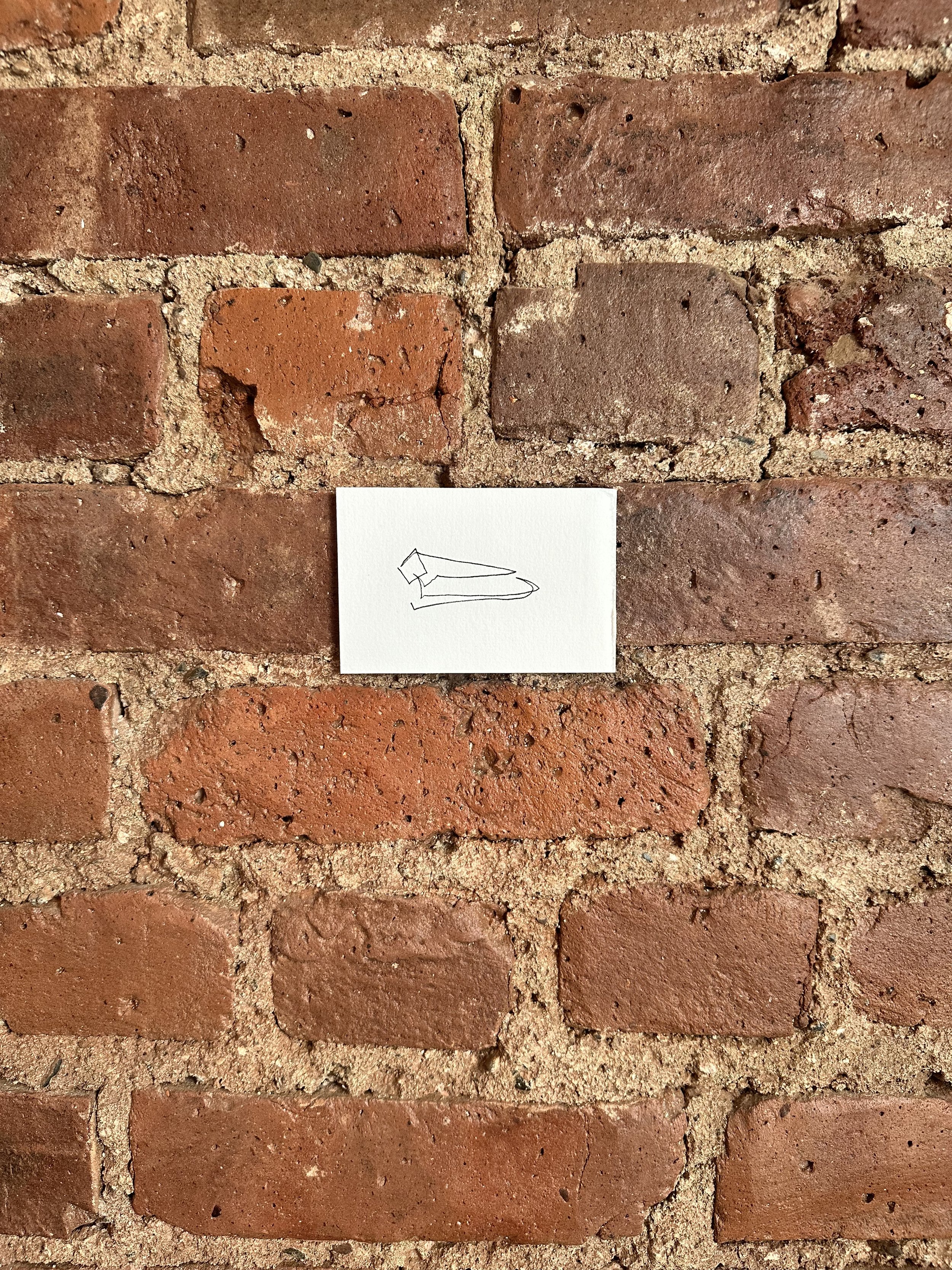 A small piece of white paper with a simple line drawing of a person lying down is attached to a brick wall.