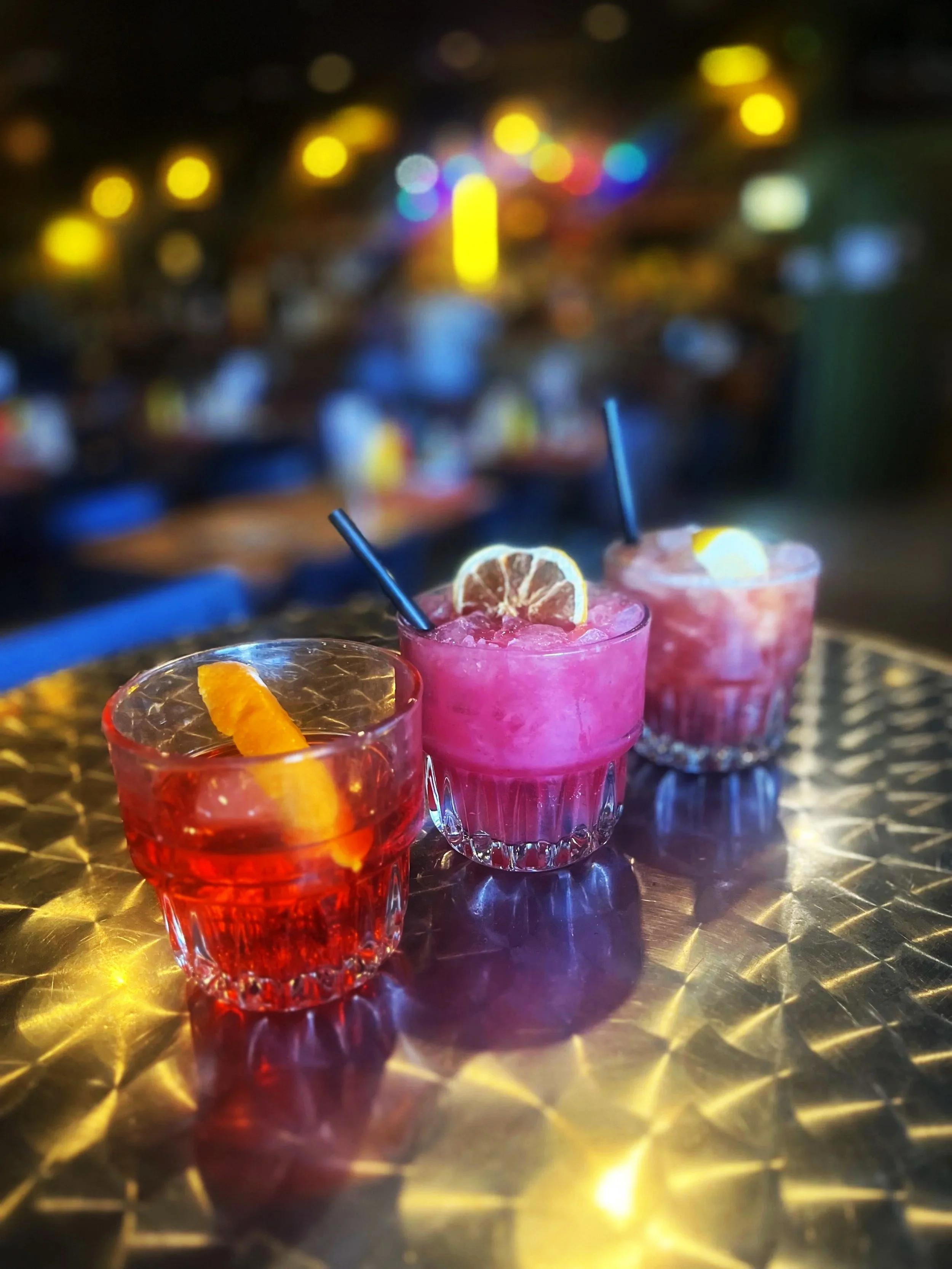 Three drinks in rocks classes, a negroni w/ orange peel, and two refreshing looking cocktails with deep berry colors and lemon slices