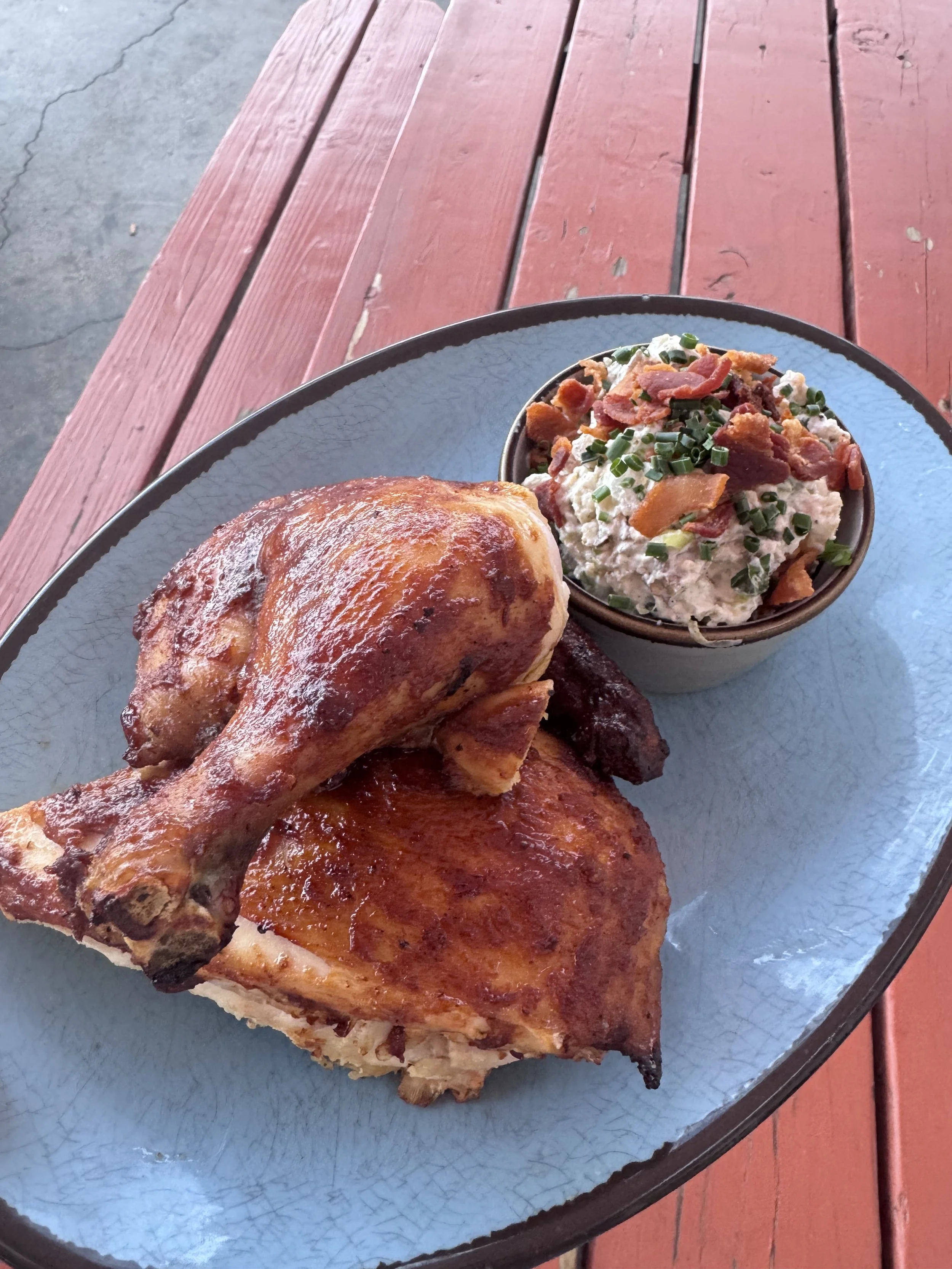 A blue plate featuring barbecued chicken and potato salad with bacon bits