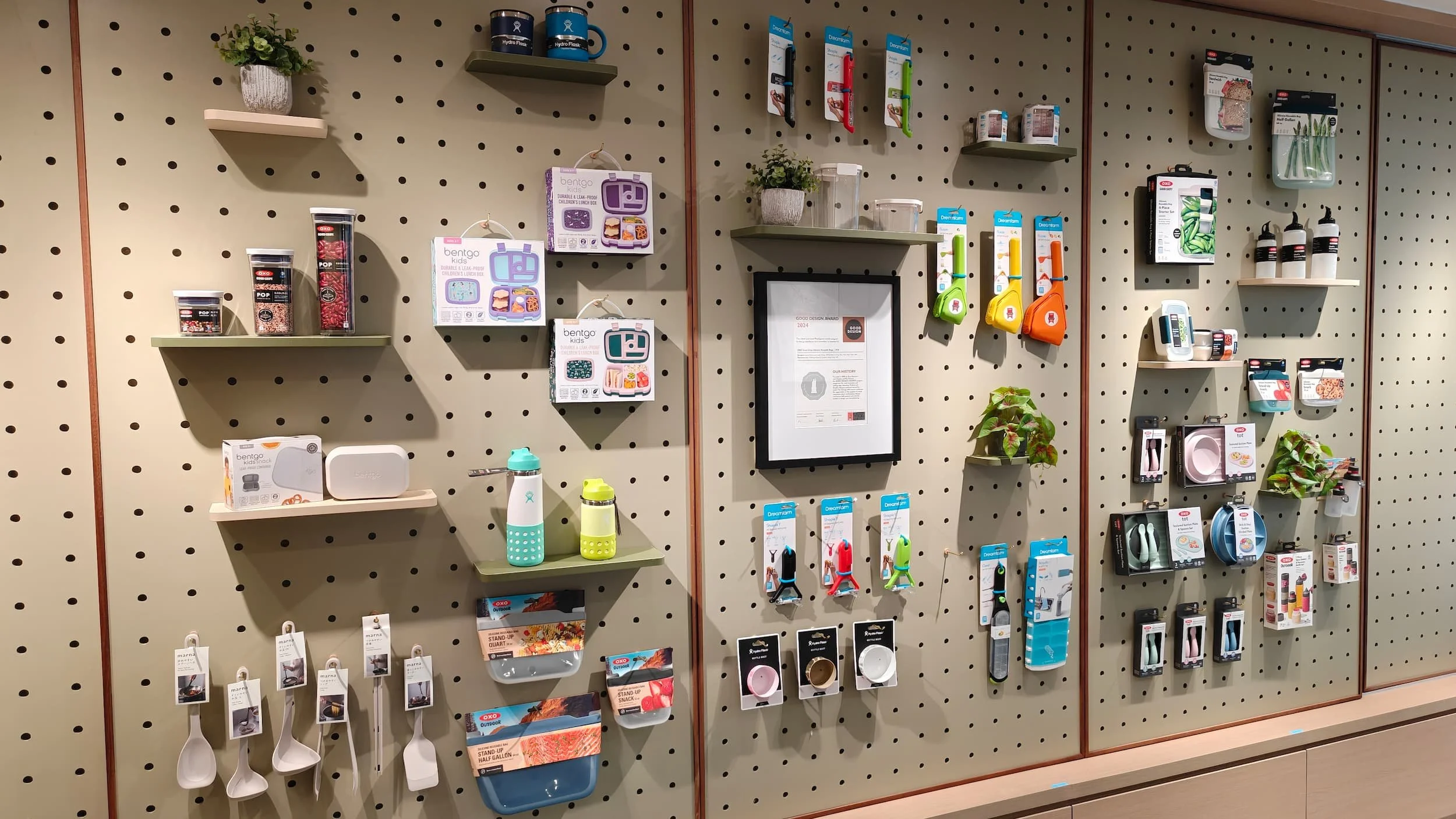 Display wall showcasing various household and kitchen items, including water bottles, kitchen utensils, plant pots, and small home decor accessories arranged on shelves and hooks.
